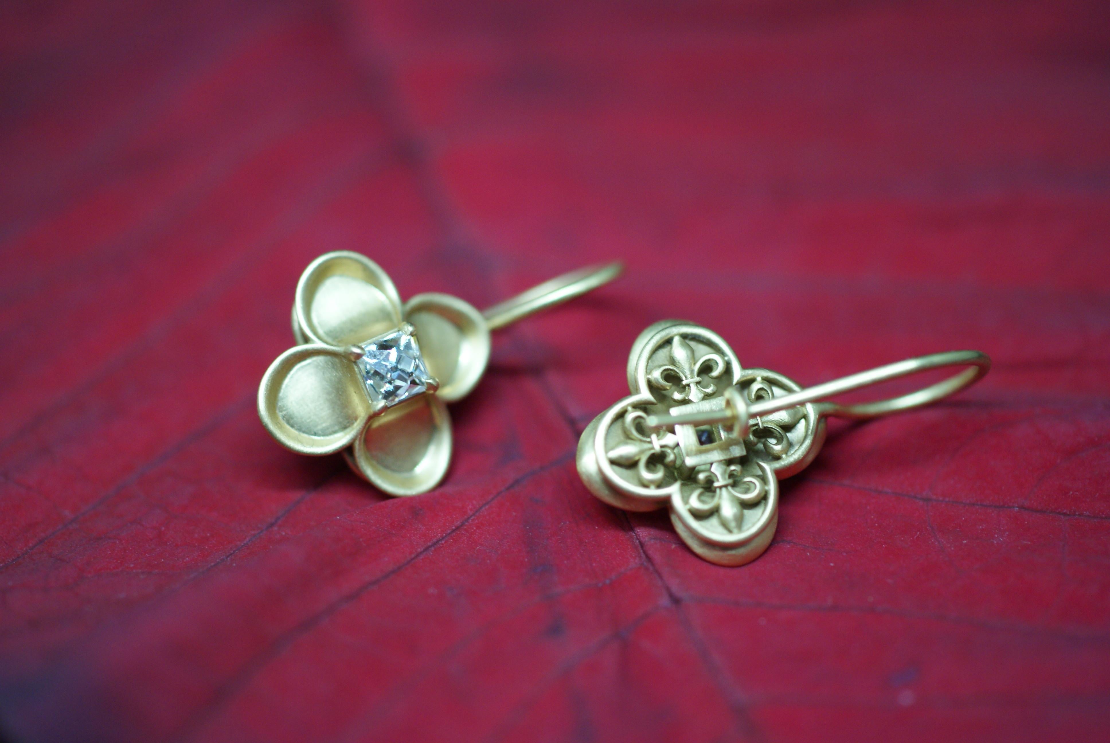 Each earring centering upon a French-cut diamond, within a stylized Renaissance Revival 'petal' setting, the reverse of each earring designed as a 'Fleur-de-lis' pattern in the quatrefoil style. These earrings are mounted in 18K gold and were made