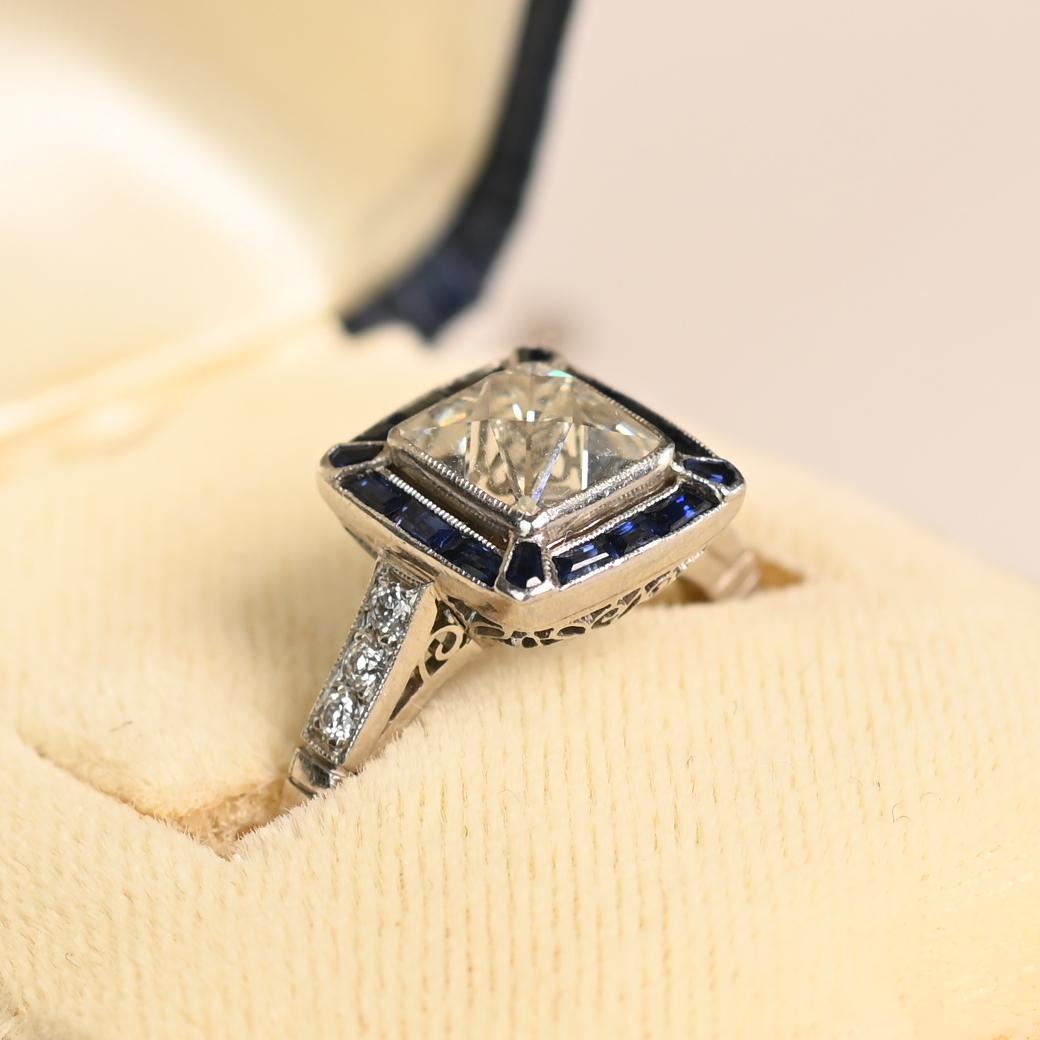 Este exquisito anillo de compromiso con halo de zafiro exhibe un impresionante diamante de talla francesa antigua certificado por el GIA de aproximadamente 1,60 quilates. Con un color J y una claridad SI1, la piedra central desprende encanto y