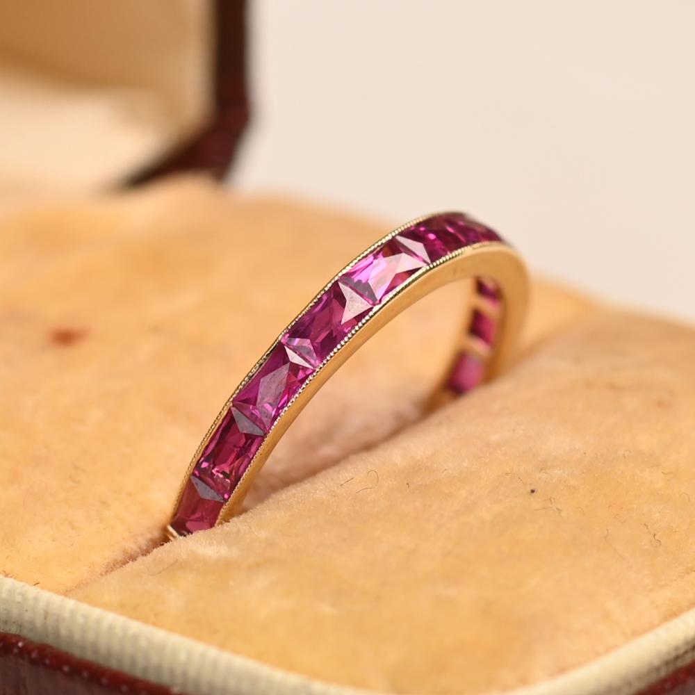 This elegant half-eternity wedding band features a vibrant row of French cut rubies, precisely arranged in a sleek channel setting. The richly hued rubies have a combined weight of approximately 1.3 carats, offering a striking pop of color against