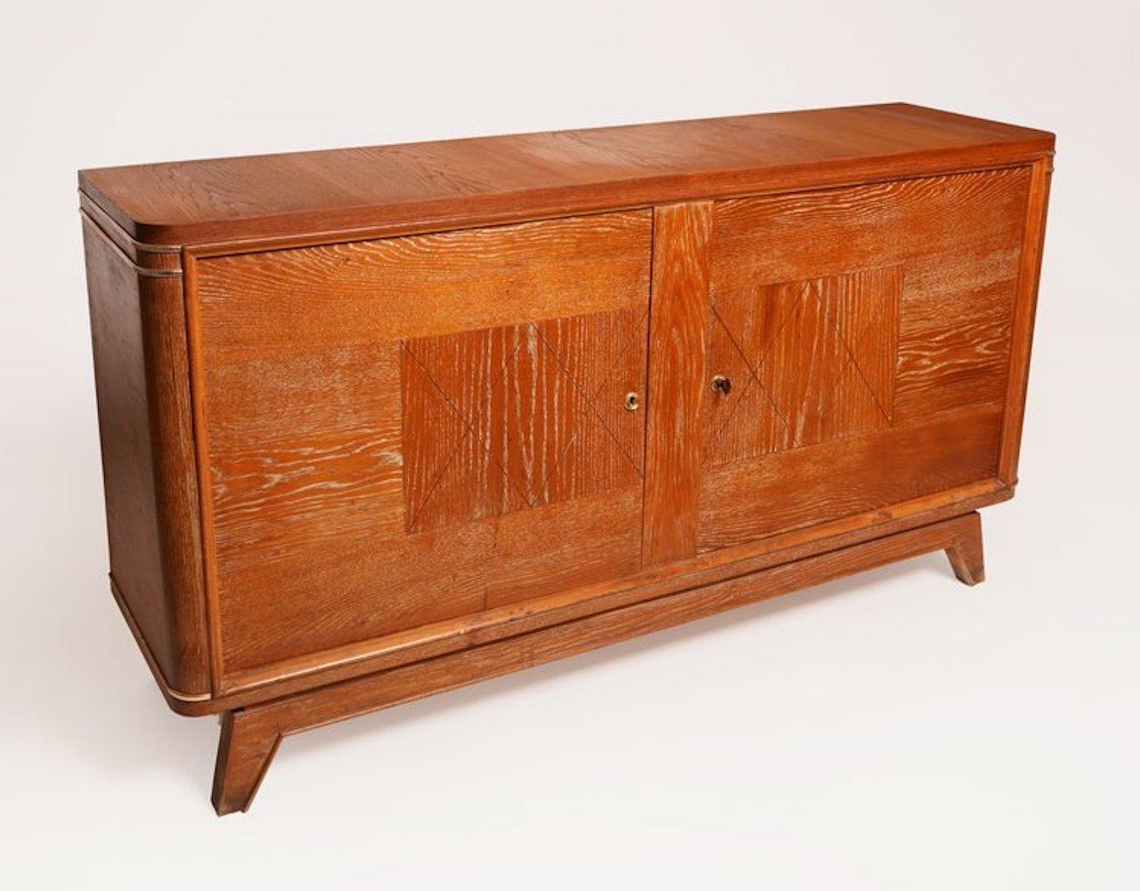 French Deco cerused oak sideboard in the style of Jean-Charles Moreux with two doors that open to reveal two small drawers and two shelves. Comes with two locks and a key. The natural cerused oak color is warm and golden.