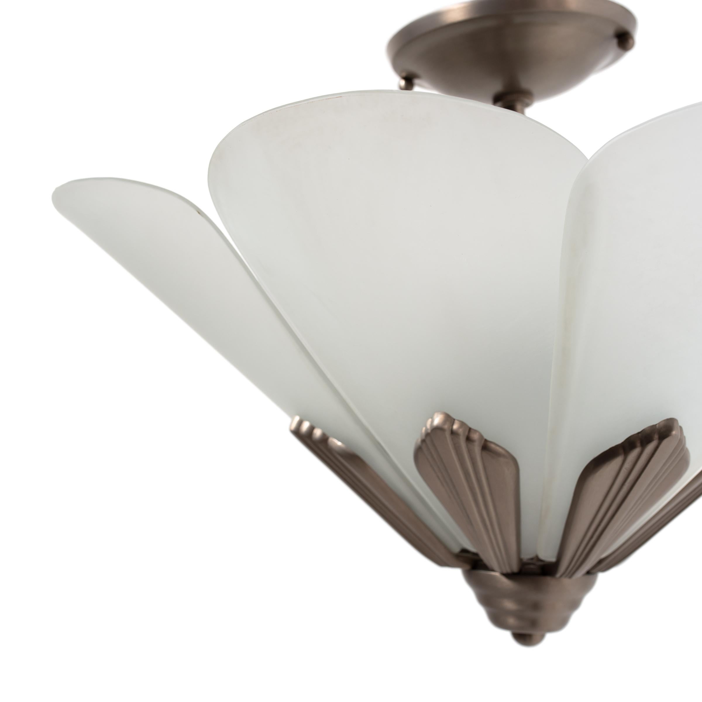 This refined frosted glass pendant light combines bold geometric metalwork with the soft refinement of French Art Deco art glass. The fixture has a conical, tapered form comprised of petal-form frosted glass shades seated in a nickel-plated bronze
