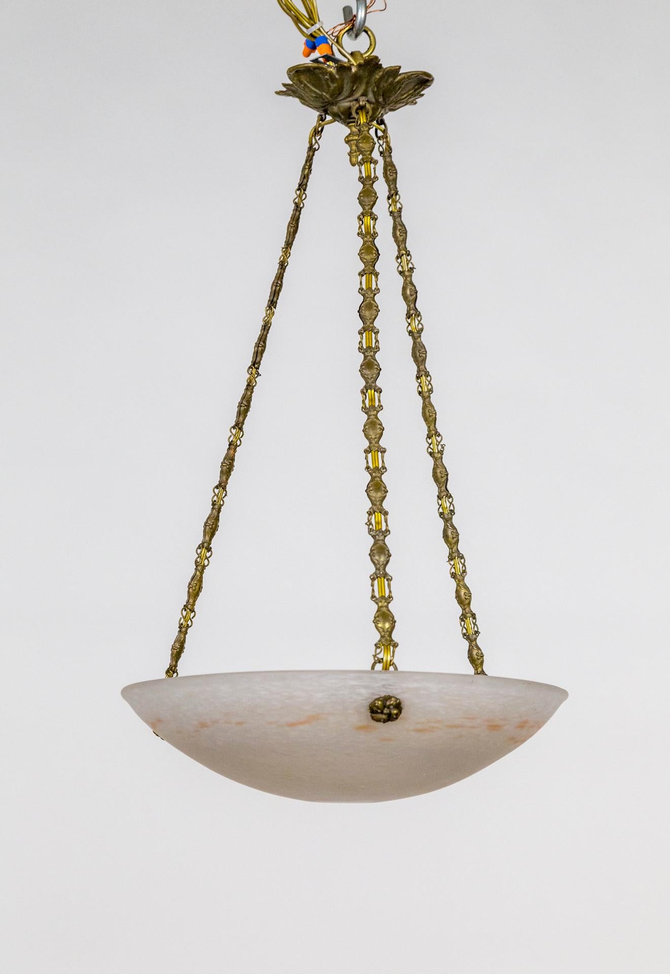 A mottled, art glass pendant in a small, shallow bowl shape by Charles Schneider. The white class speckled with subtle coral color streaks around edge. Ornate brass hardware, floral button glass holders, unique chain, and leaf canopy. Signed by the