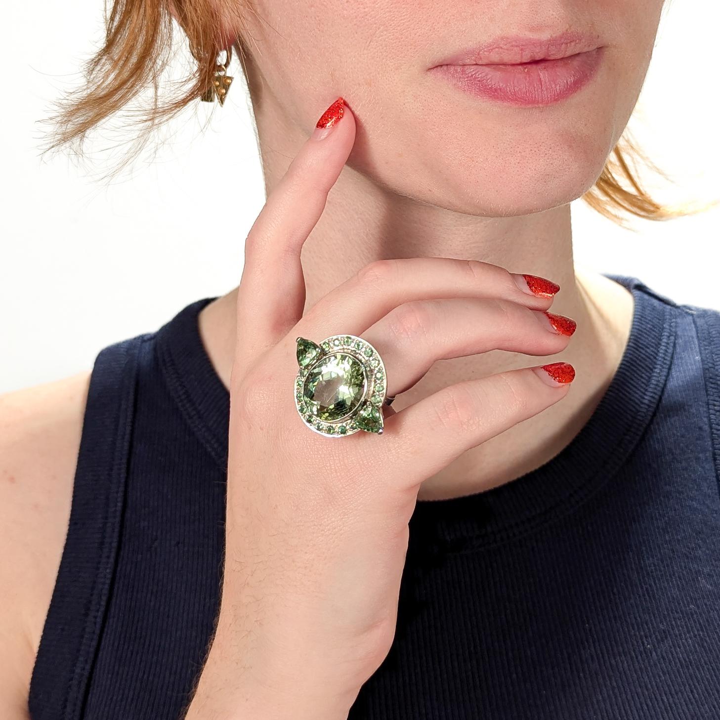 A fine French Art Deco style cocktail ring.

In 18 karat white gold.

Bezel-set with an approximately 18.5 ct oval cut green beryl gemstone. The barrel is flanked by 2 faceted triangular and a halo of green tsavorite garnet gemstones. Supported by a
