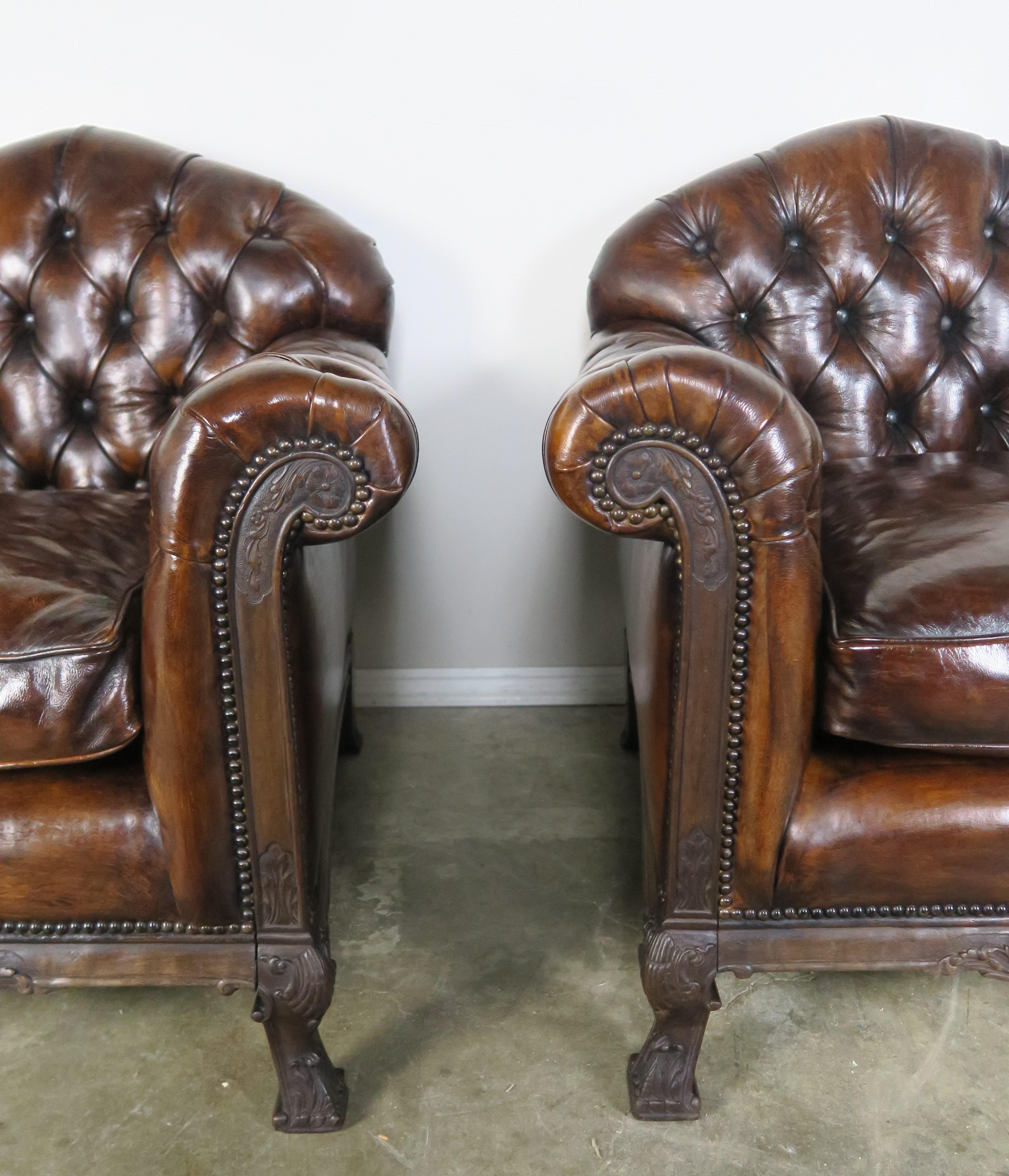 Pair of French Deco style leather tufted armchairs with loose seat cushions. Carved walnut frame with beautiful details on the front and feet of the chairs. Great patina on leather and finished in antique brass colored nailheads around the frame of