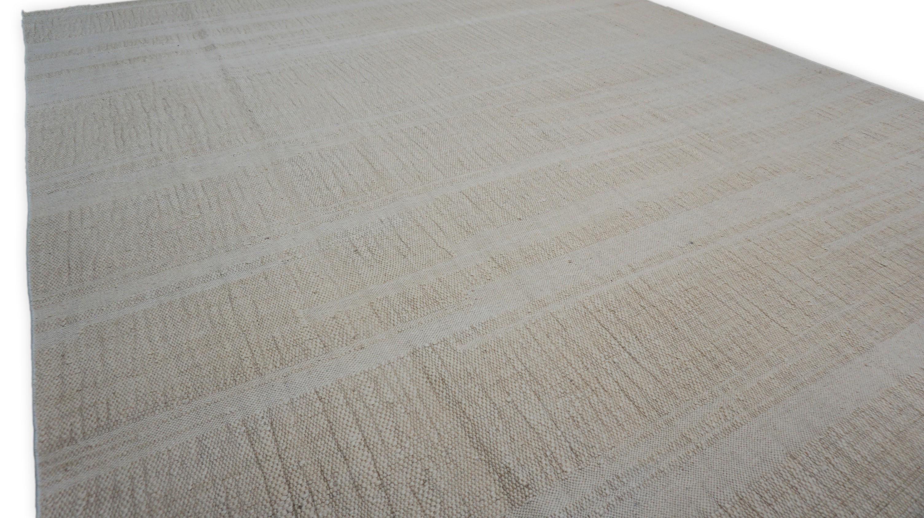 Dieser flachgewebte Wollteppich weist ein subtiles, strukturiertes Streifenmuster auf, gewebt in einem weichen, warmen Hellbraun, Beige und Elfenbein,  Palette mit zarten Klangfarbenvariationen. Die fein gearbeiteten horizontalen Streifen sorgen für
