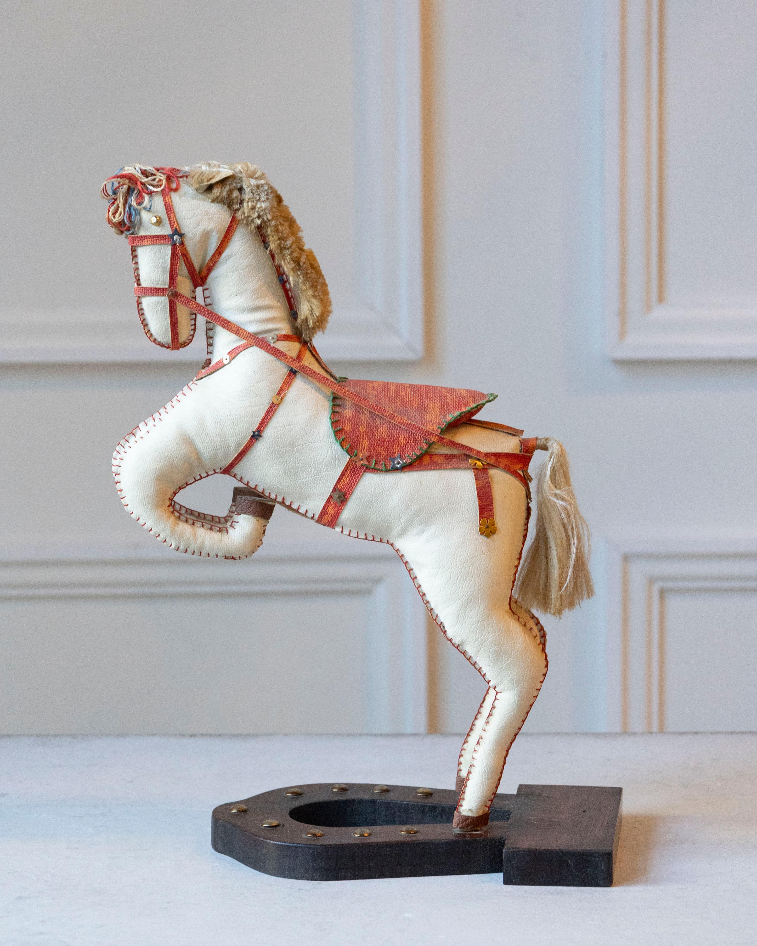 Charming and sculptural, this French decorative horse from the 20th century captures the elegance and vitality of equestrian form. Covered in soft moleskin, the figure rests on a black horseshoe-shaped wooden base and is poised in a rearing stance,