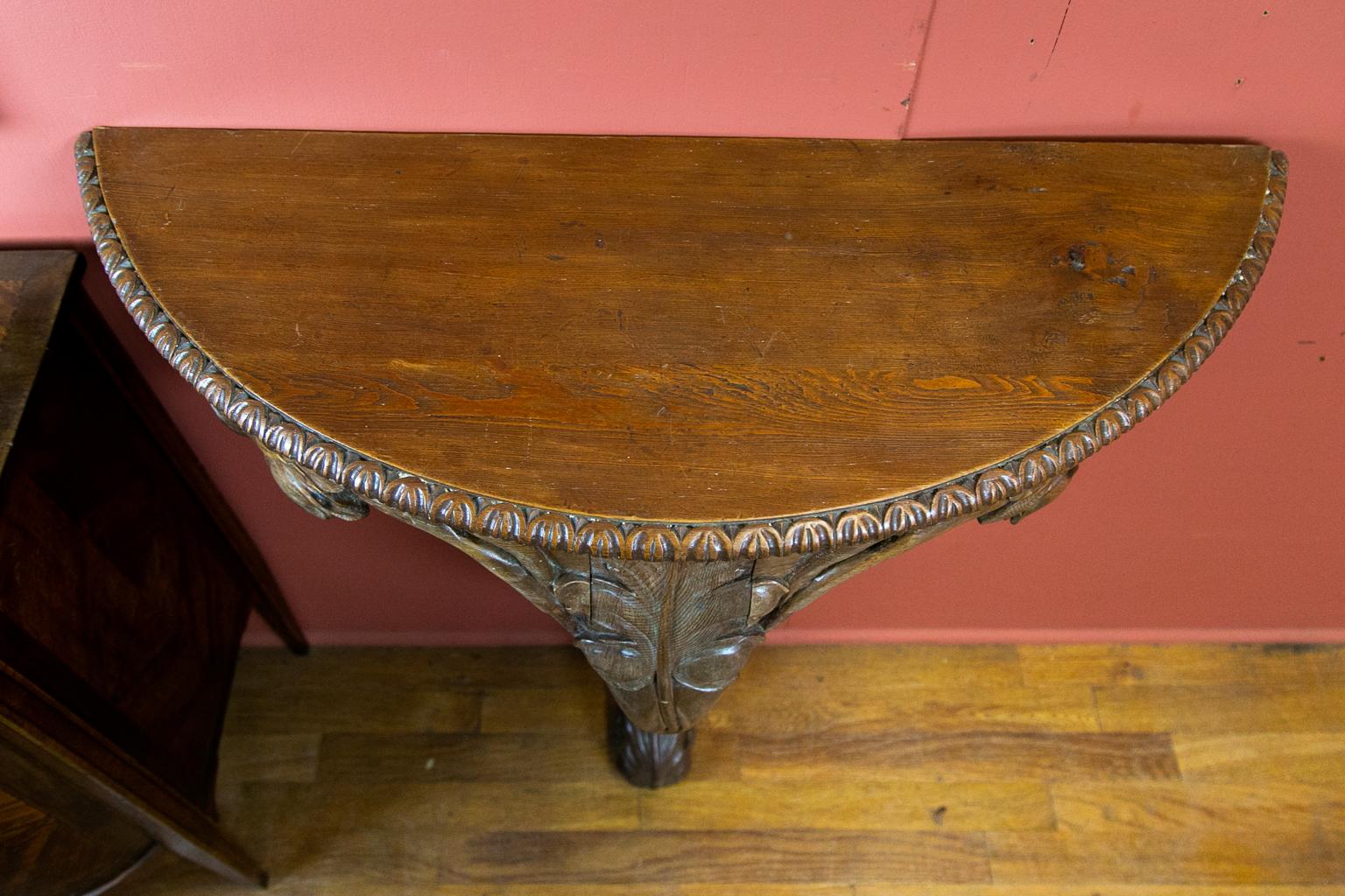 French demilune pine console table, the top having carved molding of a stylized egg and dart. The base has carved leaf and twig designs terminating in a vertical acanthus leaf foot.