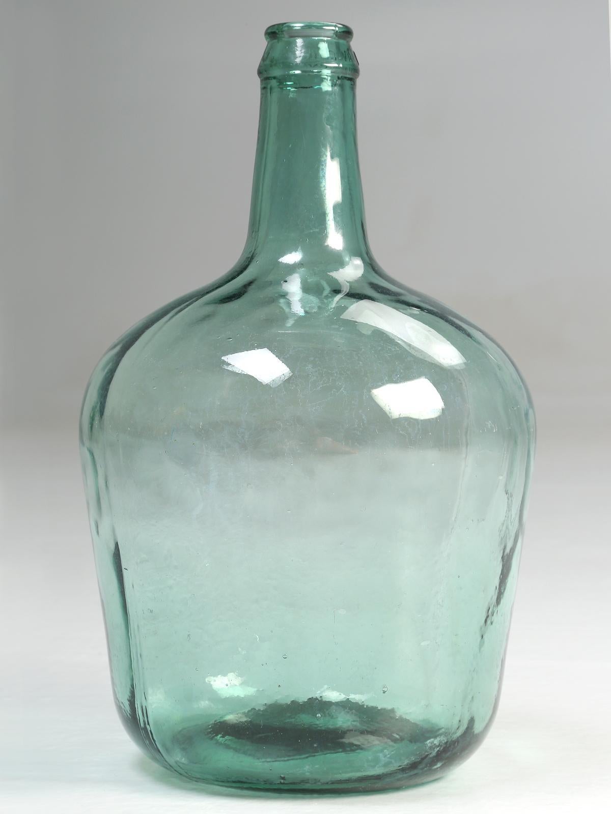 Demijohn and carboy were often used to describe the same glass bottle. The difference seems to be more of its function than form. Carboys were used to transport strong chemicals, while Demijohns were used for non-corrosive fluids. 
The top, around