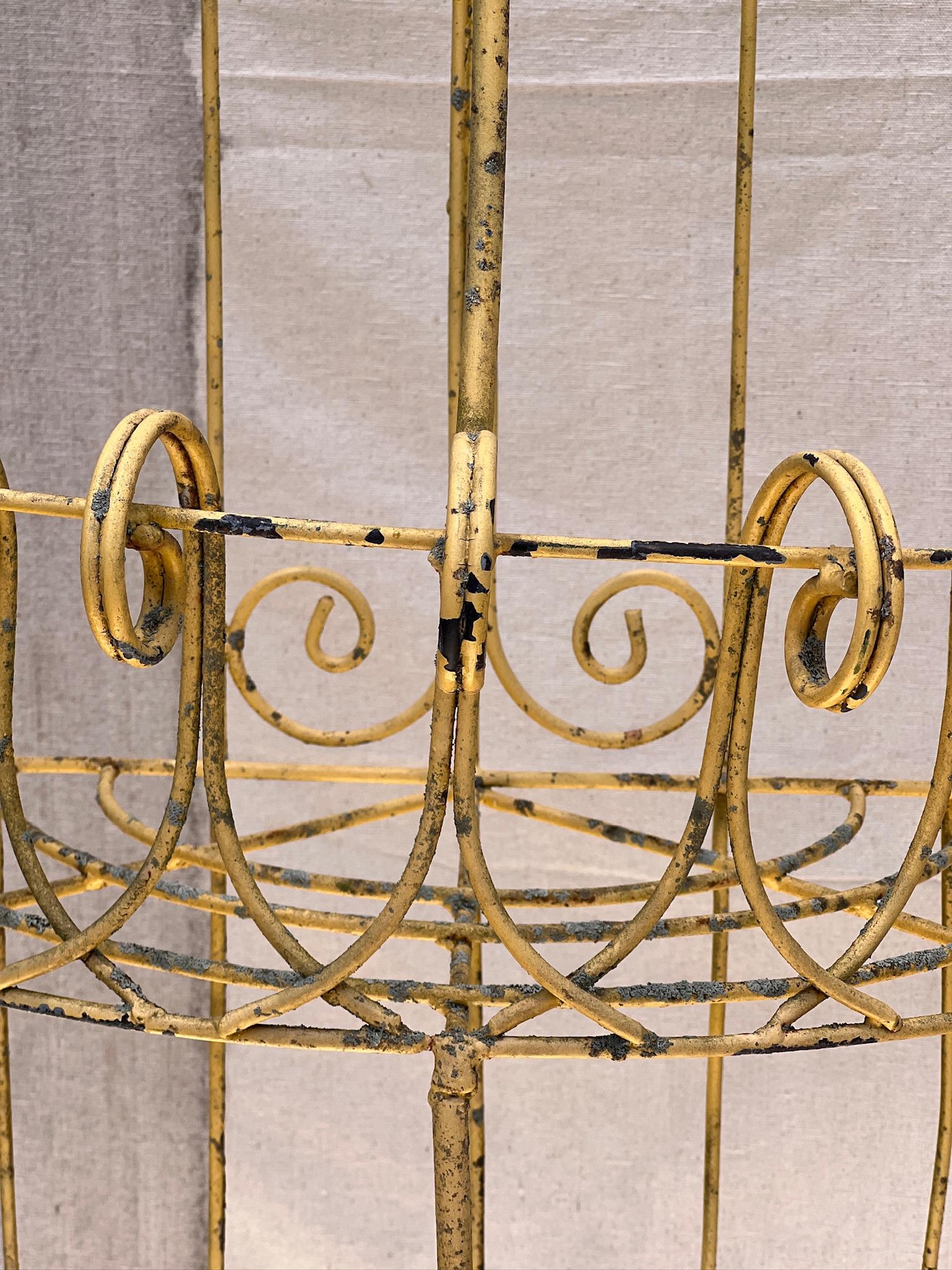 A magnificent French plant stand with three tiers, featuring an elegant demilune design. The iron frame of the stand is adorned with gracefully scrolled wire borders on each shelf. It stands on three sets of legs, each culminating in scrolled feet,