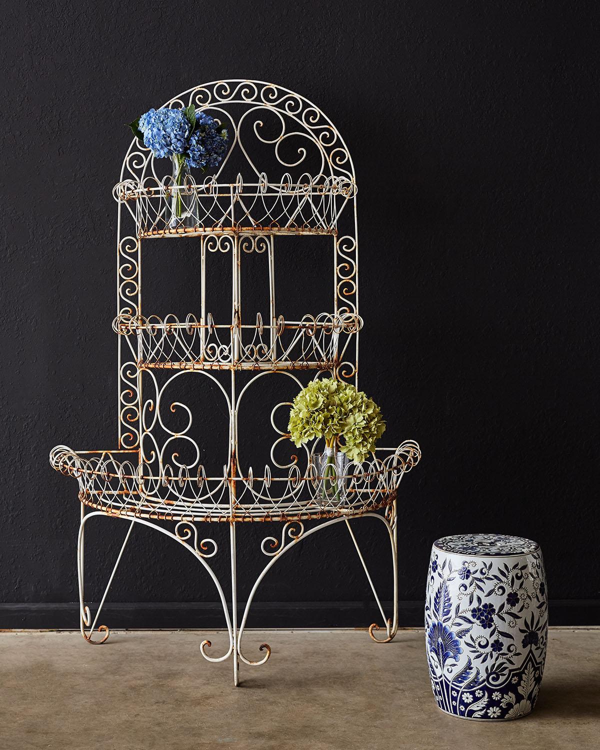 Grand French three-tier iron and wire plant stand having a demilune form. The three tier iron frame is decorated with wire bent in a graceful scrolled border on each shelf. Supported by three sets of legs ending with scrolled feet. Excellent joinery