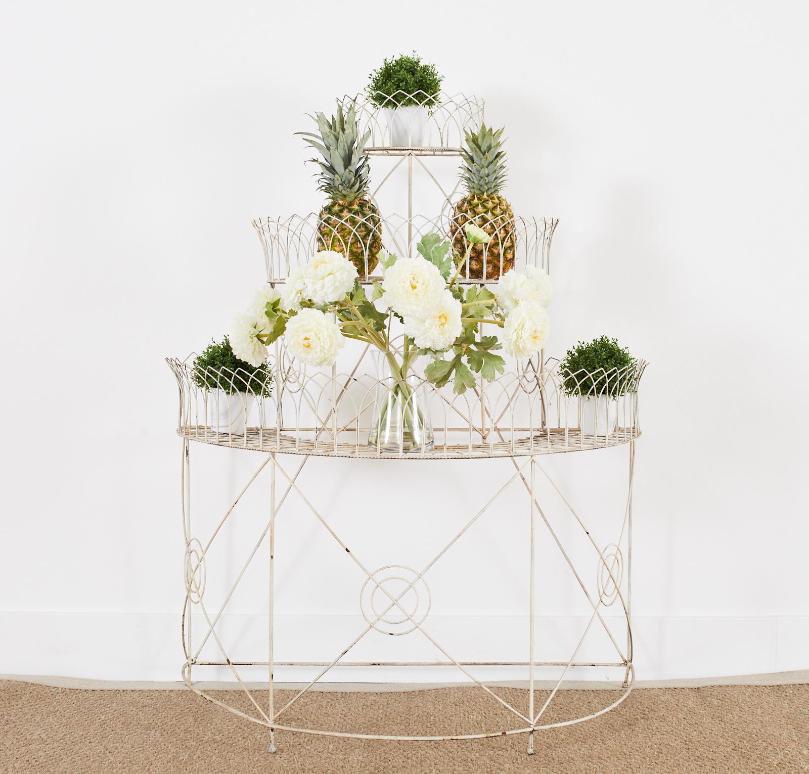 Charming French three-tier iron and wire plant stand having a demi-lune form. The three tier frame is decorated with faux-rope border on each shelf and graceful pointed arches. The base is supported by four legs decorated with a target motif design