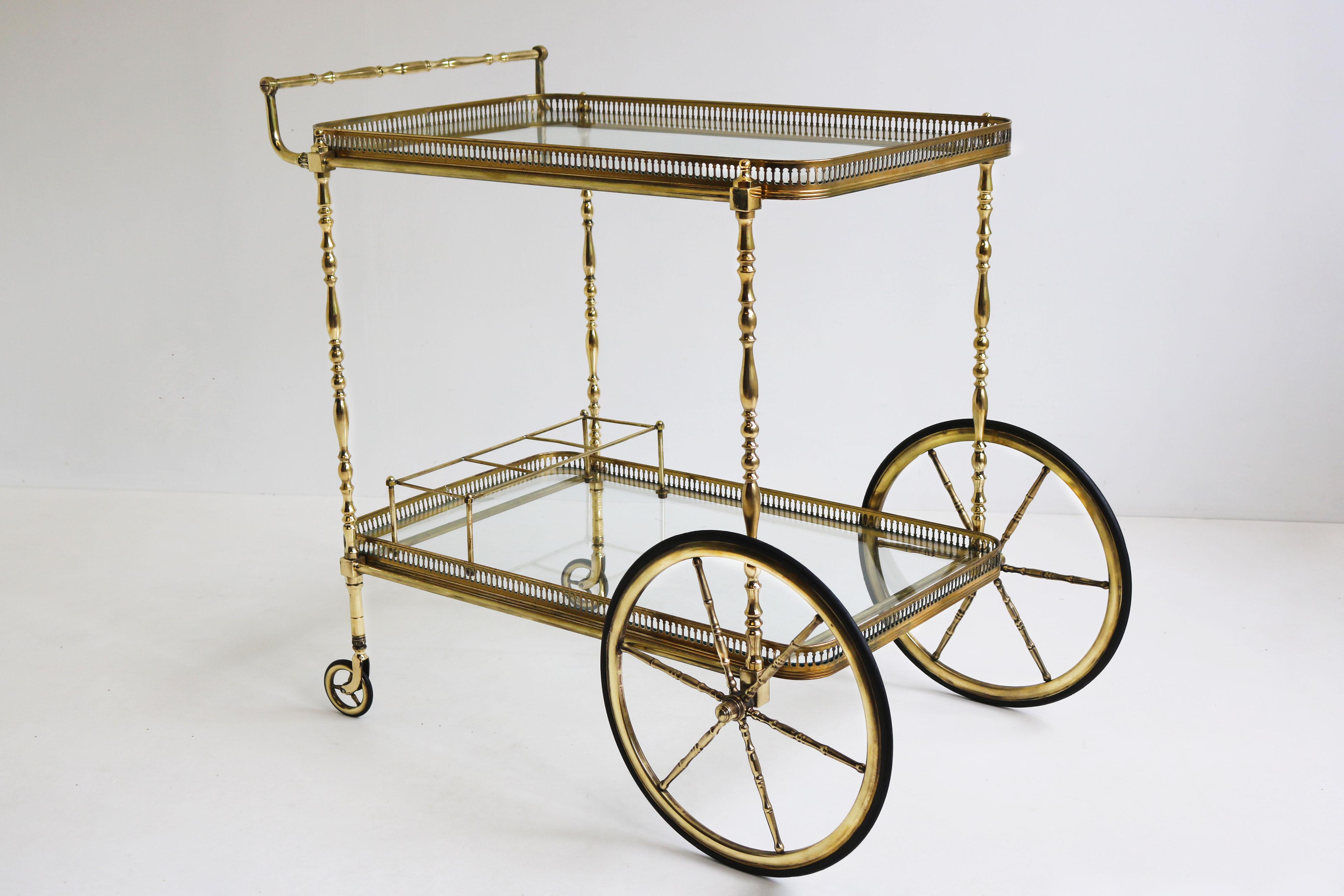 Gorgeous full brass neoclassical bar cart / serving trolley designed by Maison Bagues in 1940. An exquisite quality piece, that radiates luxury. 
The bottom of the bar cart has a bottle holder. 
The bar cart has 2 glass shelves, perfect for