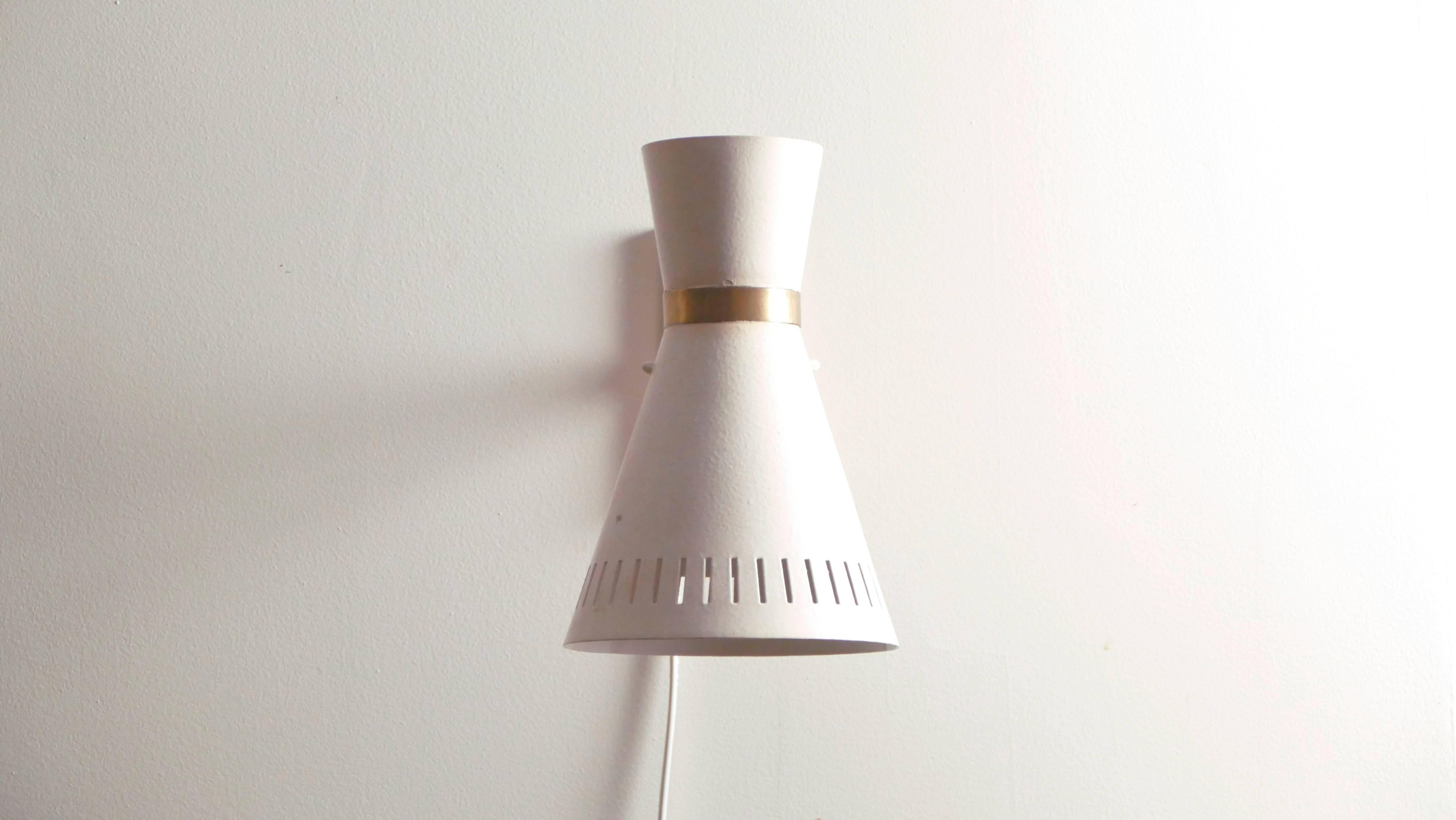 This 1960s sconce was modeled in the style of French designer Pierre Guariche, exhibiting a minimalistic midcentury modern look. The light fixture is made of brass and white metal and shaped in an uneven diabolo form that feels at once timeless and