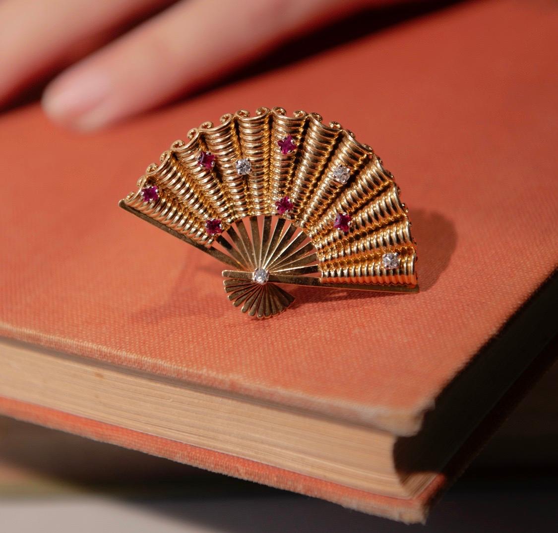 An 18 carat gold whymsical fan brooch with a ribbed fabric set with six carré cut rubies and four brilliant cut diamonds, French, circa 1960. 

weight: 10.5 grams
length: 4.5 cm

Provenance: collection Juliette Gréco, French actress and singer who
