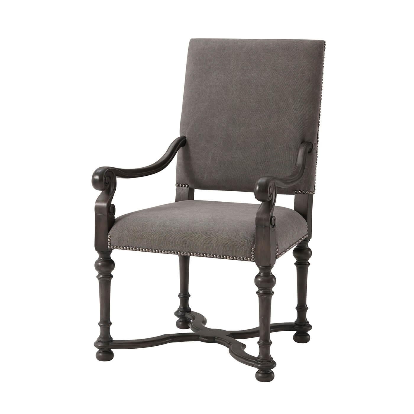 A Louis XIV style French dining chair with a square padded and upholstered backrest and seat, with carved scrolling arms, on turned legs with an X-stretcher base and finished with detailed antiqued brass nailheads.
Armchair dimensions: 25