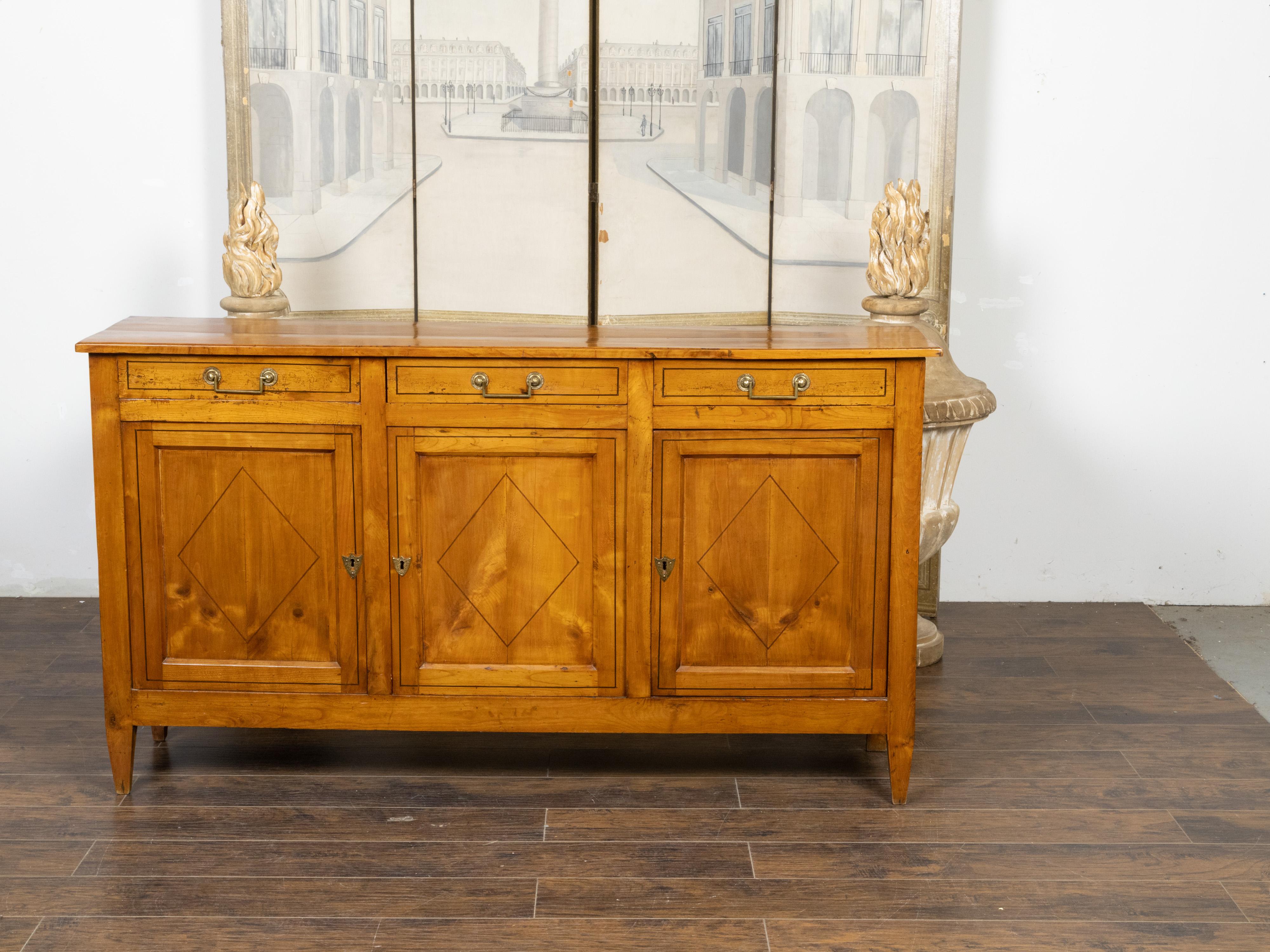 A French Directoire style walnut enfilade from the 19th century, with three drawers over three doors, cross-banded diamond motifs and tapered feet. Created in France during the 19th century, this Directoire style walnut enfilade features a