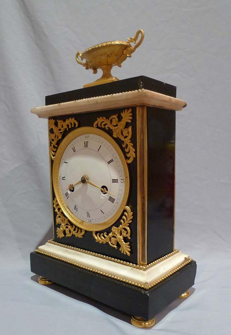 French Directoire period mantel clock. Constructed of black marble with white statuary marble mouldings with fire gilt/mercury ormolu touches such as feet, beading, chamfered corners, spandrel mounts, bezel and classical urn this is a really smart