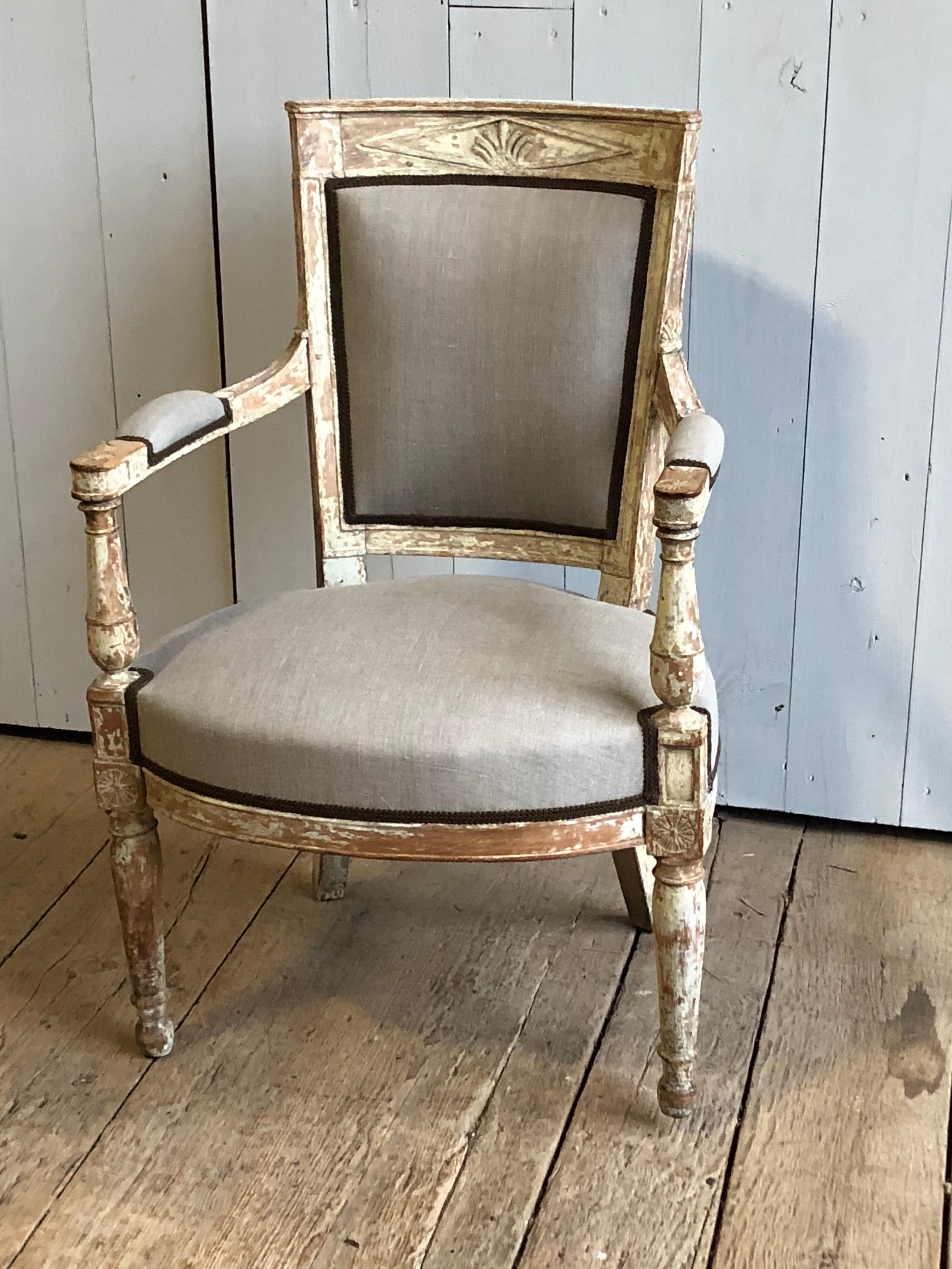 A French neoclassic Fauteuil, Directoire period, circa 1800 with newly upholstered seat and back in grey linen and brown gimp. Original painted finish with carved back rail and armrests. Measures: Arm height 24.5”.