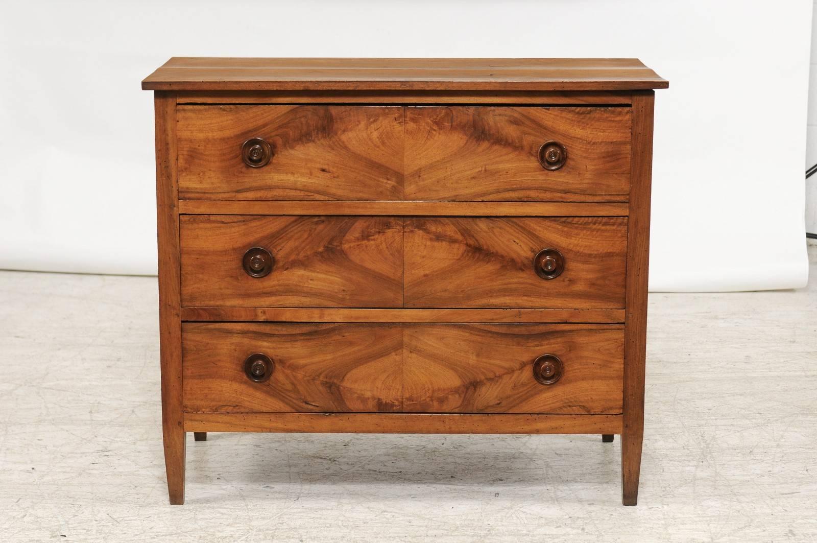 A French Directoire period three-drawer commode with bookmarked walnut veneer from the late 18th century. This French commode was born in the later years of the 18th century, during the troubled times that followed the French Revolution. The chest
