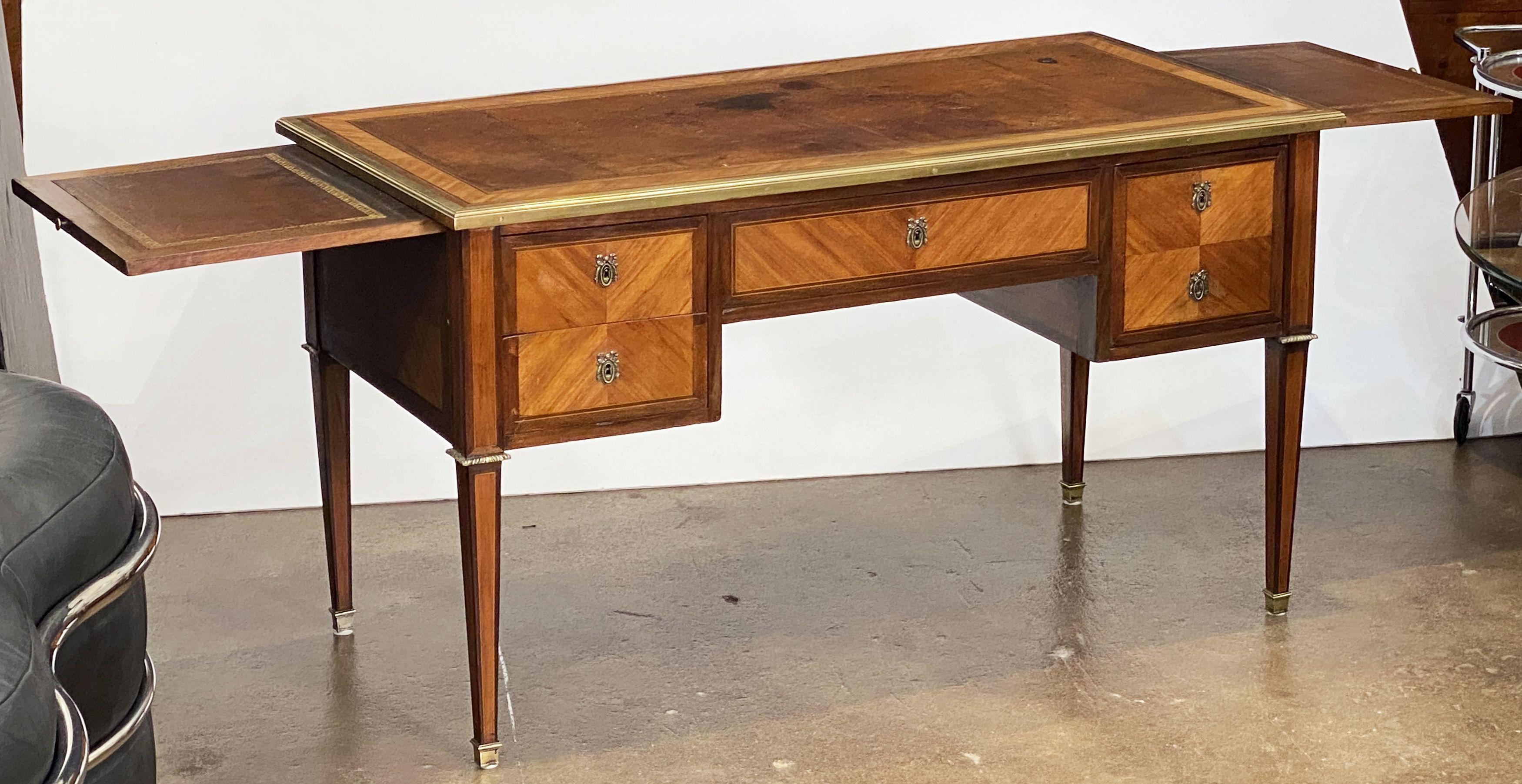 A fine French Directoire period writing table or desk of walnut and mahogany from the late 18th century, featuring an embossed leather top with brass accents, with two brushing slides and four drawers with brass escutcheons, the back with faux
