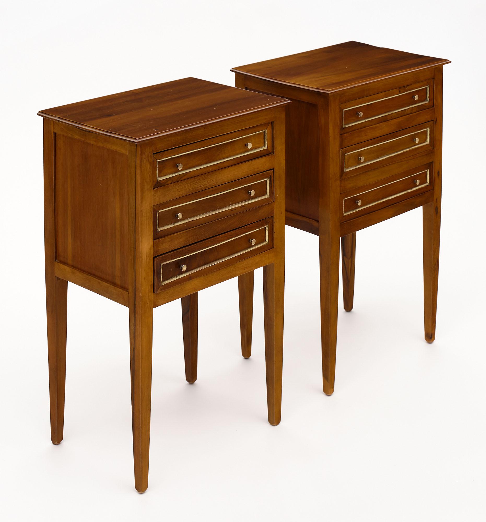 Pair of bed side tables from France made of walnut with tapered legs. Each cabinet features three dovetailed drawers all trimmed in gilt brass.