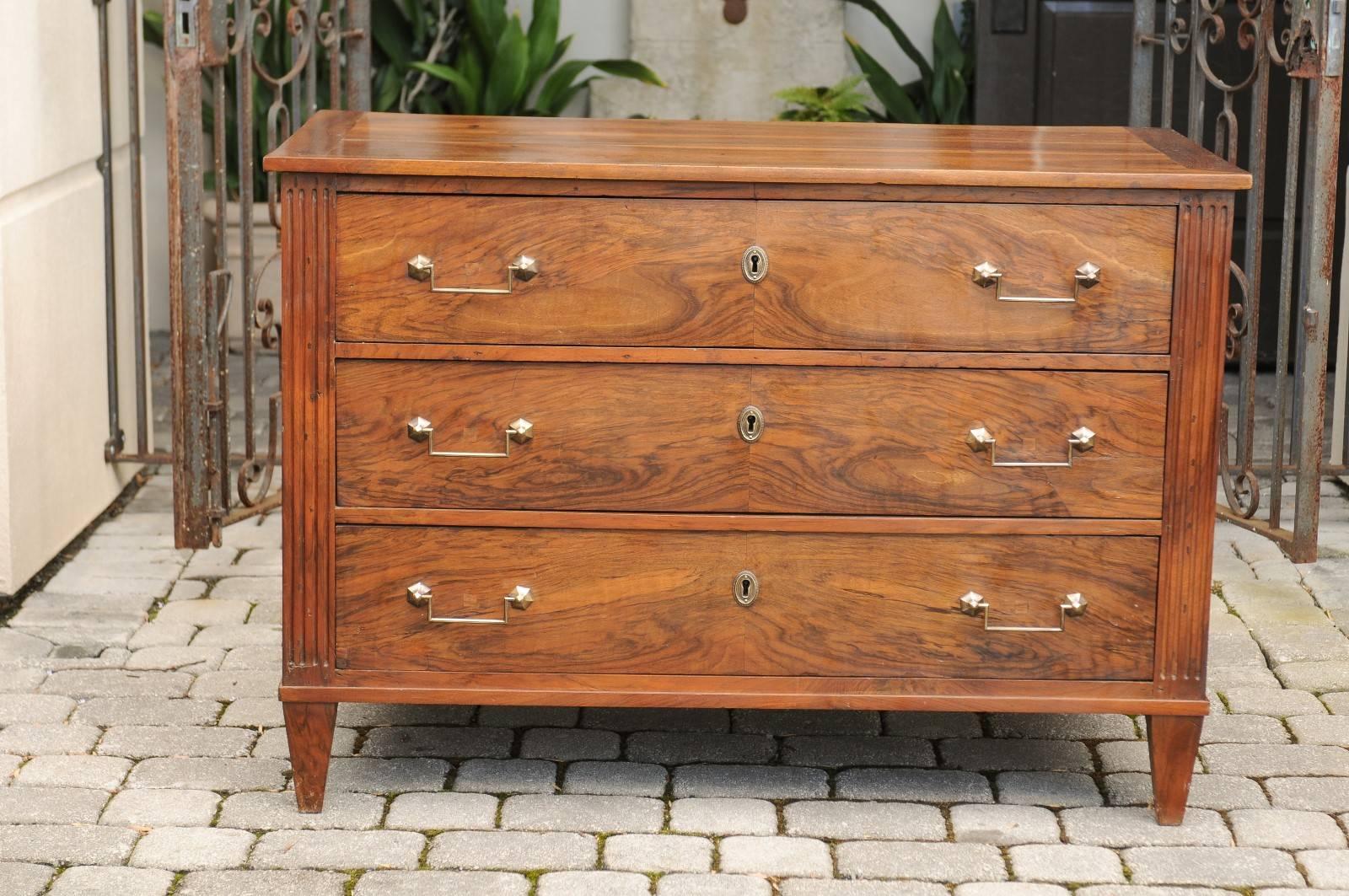 A French Directoire style three-drawer commode from the first half of the 19th century with bookmarked walnut veneer, fluted side posts and tapered feet. This French commode features a rectangular planked top sitting above three exquisite bookmarked