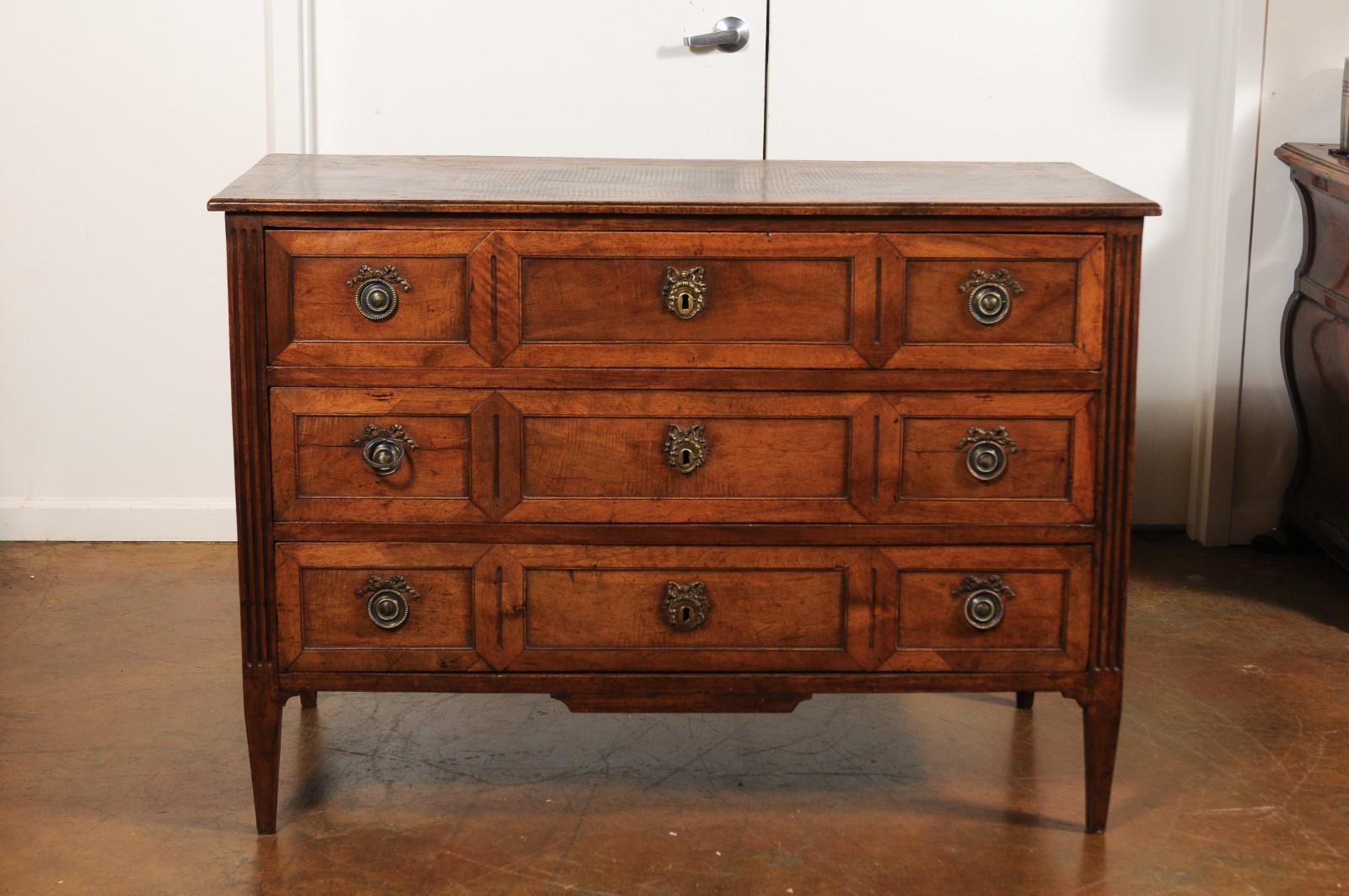 A French Directoire style walnut veneered three-drawer commode from the mid 19th century, with inlaid accents, fluted side posts and tapered legs. Born in the third quarter of the 19th century during the reign of France's last Emperor Napoleon III,