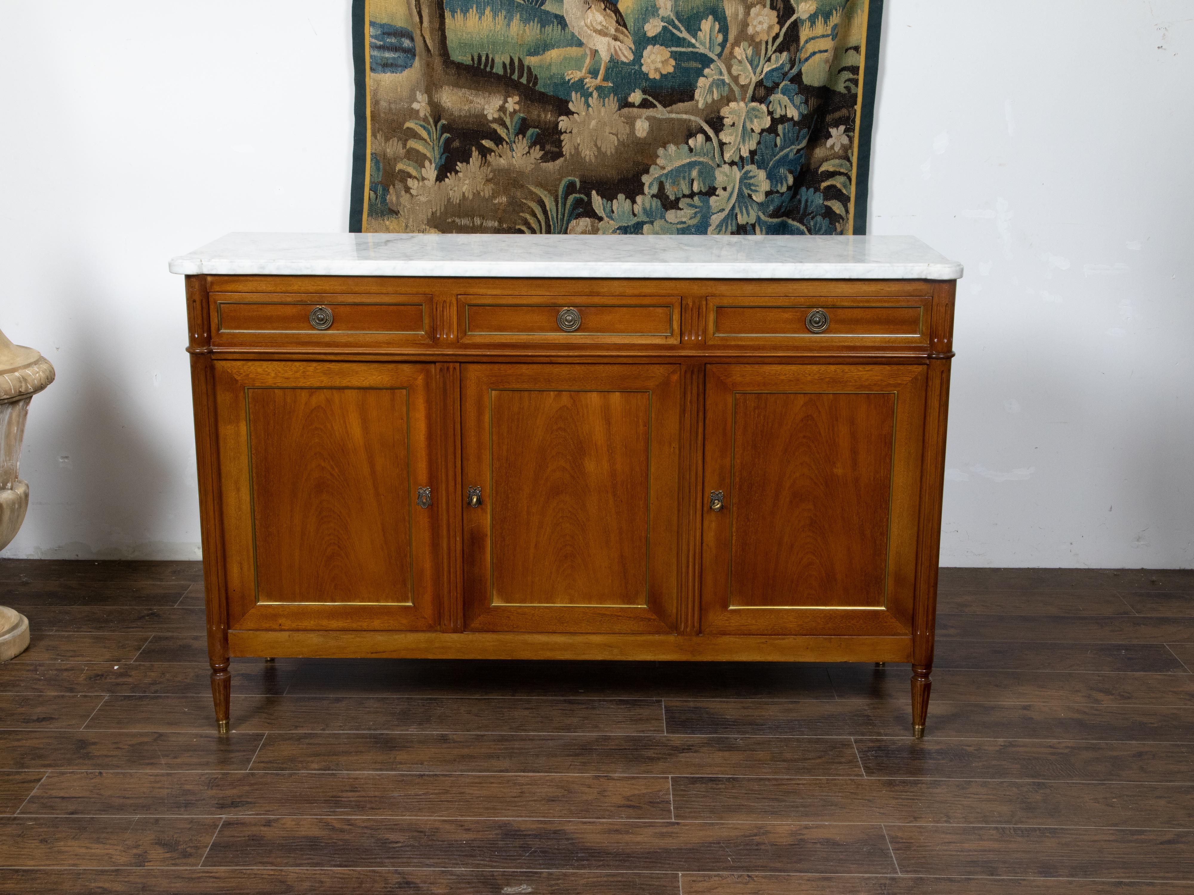 A French Directoire style mahogany sideboard from the 19th century, with white marble top, three drawers over three doors and brass accents. Created in France during the 19th century, this Directoire style mahogany sideboard features a rectangular