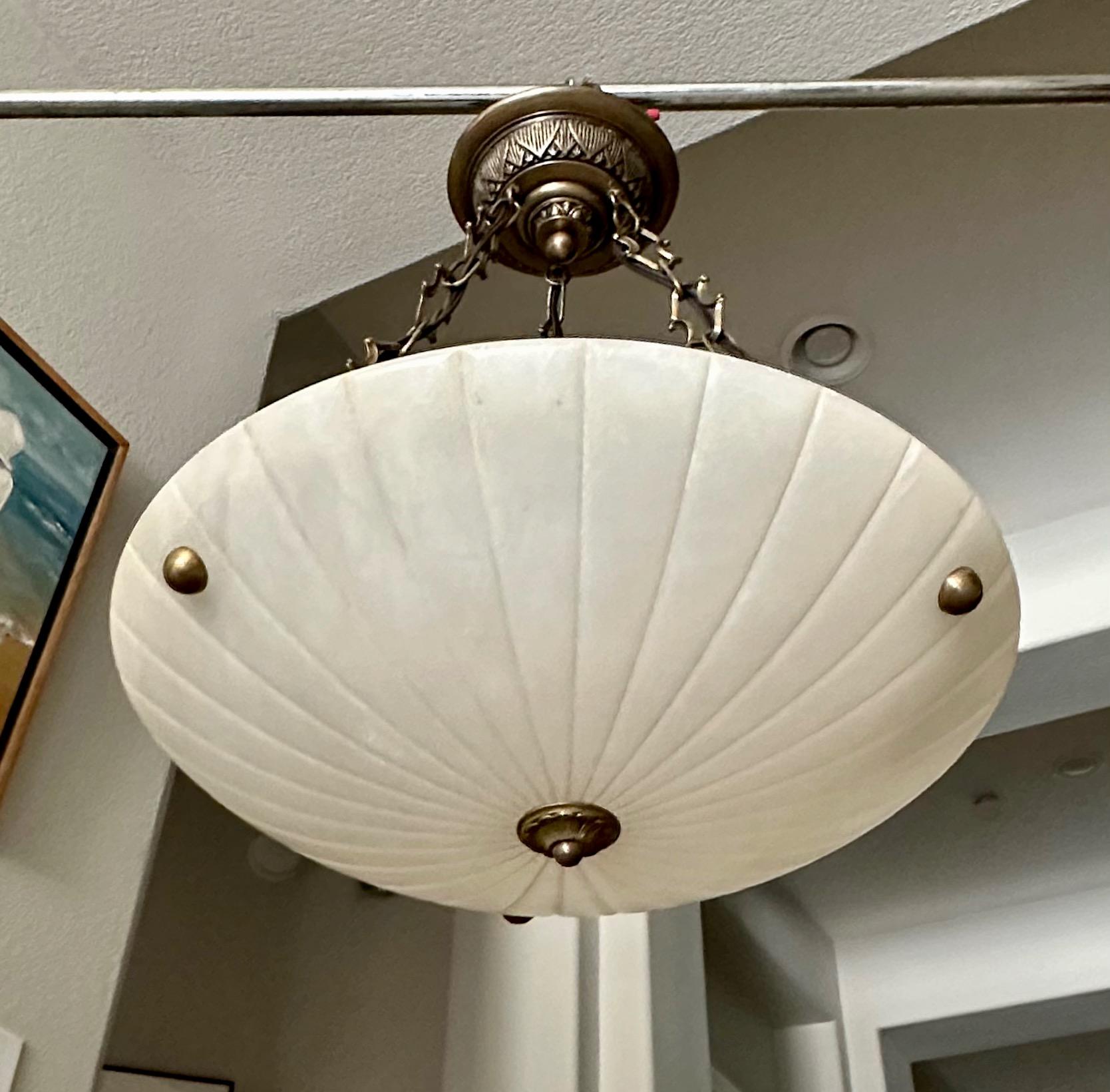 Alabaster pendant light or chandelier with aged patinated brass fittings in the Directoire style. Expertly carved with incised sunburst pattern design. Wired for US, fixture uses three regular A base bulbs. 

Measures: Alabaster is 19.75