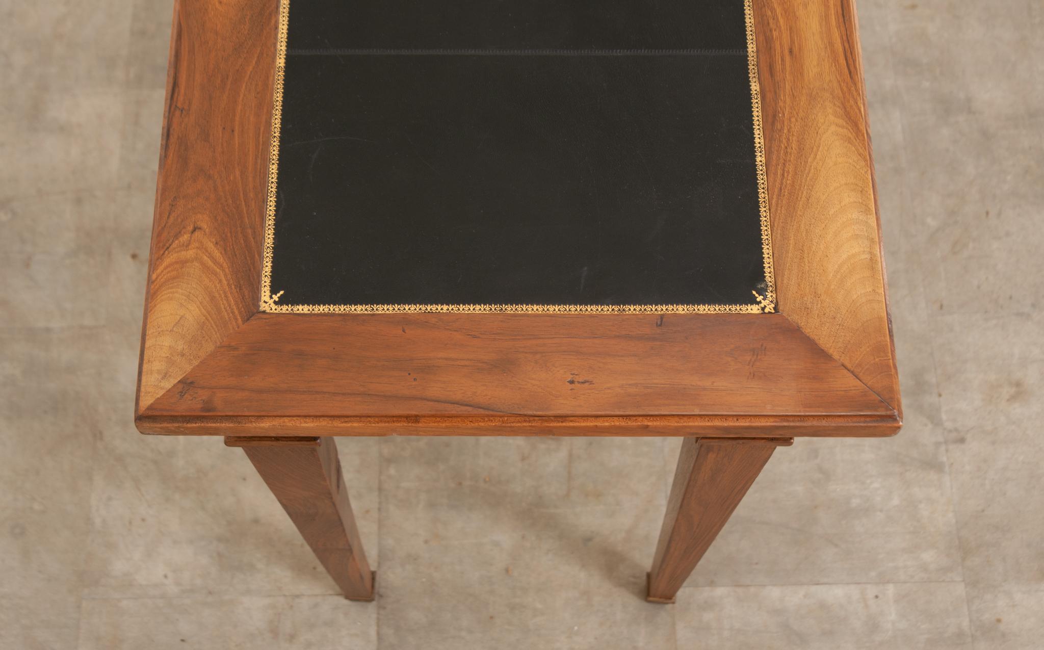 This petite writing desk made of solid mahogany is perfect for casually working or makes for a wonderful side table or console. The top features a gently worn black leather writing surface with classic gold embossed trim. There are two functioning