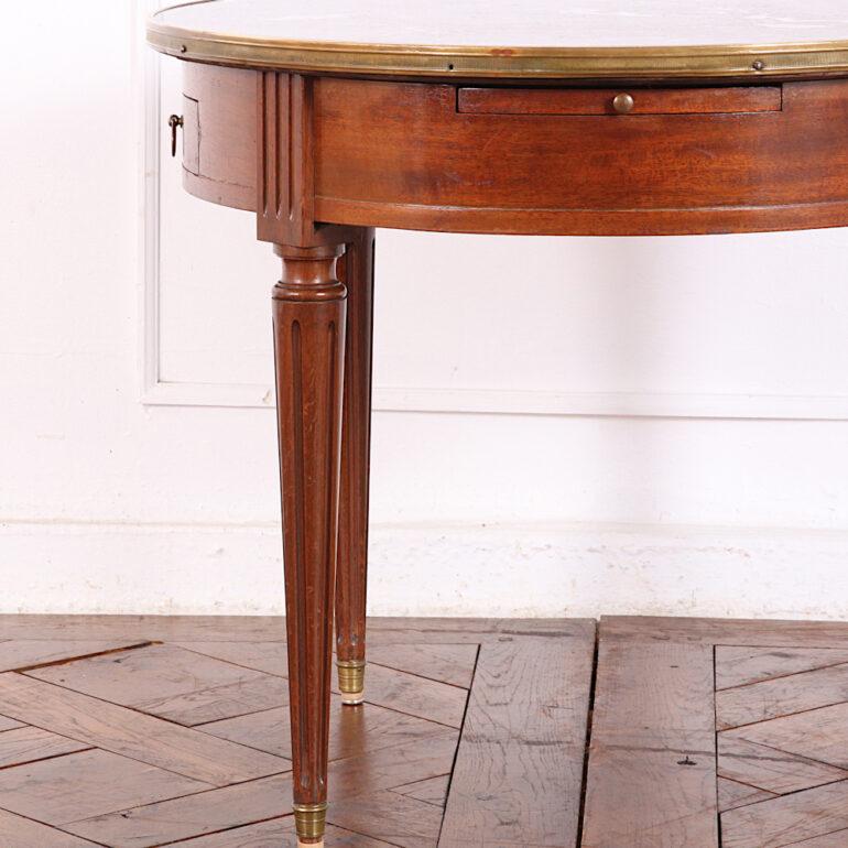 A French Directoire style round marble top coffee or occasional table with two small drawers and two pull-out surfaces fitted to the skirt and with a brass edge to the flecked grey marble top. Raised on elegant turned tapering and fluted legs. C.