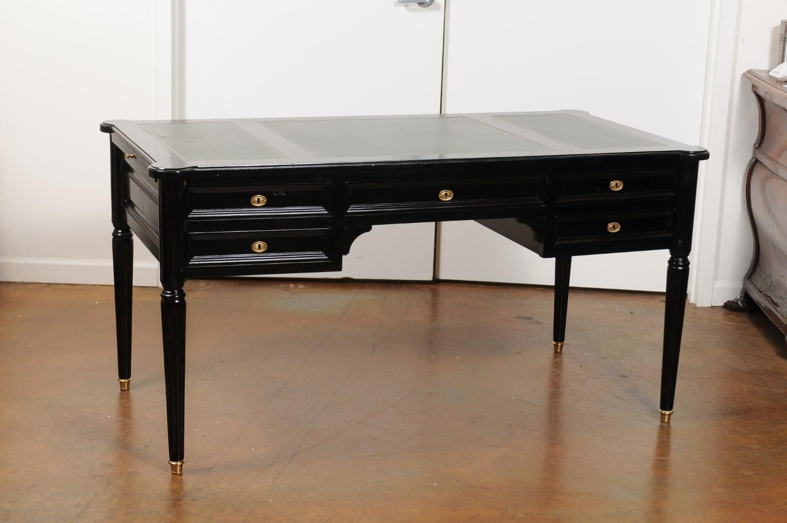 A French Directoire style ebonized wood five-drawer desk from the mid-20th century, with green leather writing surface, brass accents and fluted legs. Born in France during the midcentury period, this exquisite desk features a rectangular top with