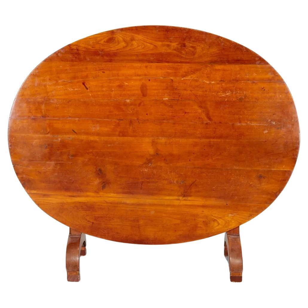 A nice quality tilt-top wine tasting table in cherry-wood, circa 1800, the oval plank top supported by turned column-form supports on arched feet, and a lyre-form rotating support for the top in its open position.