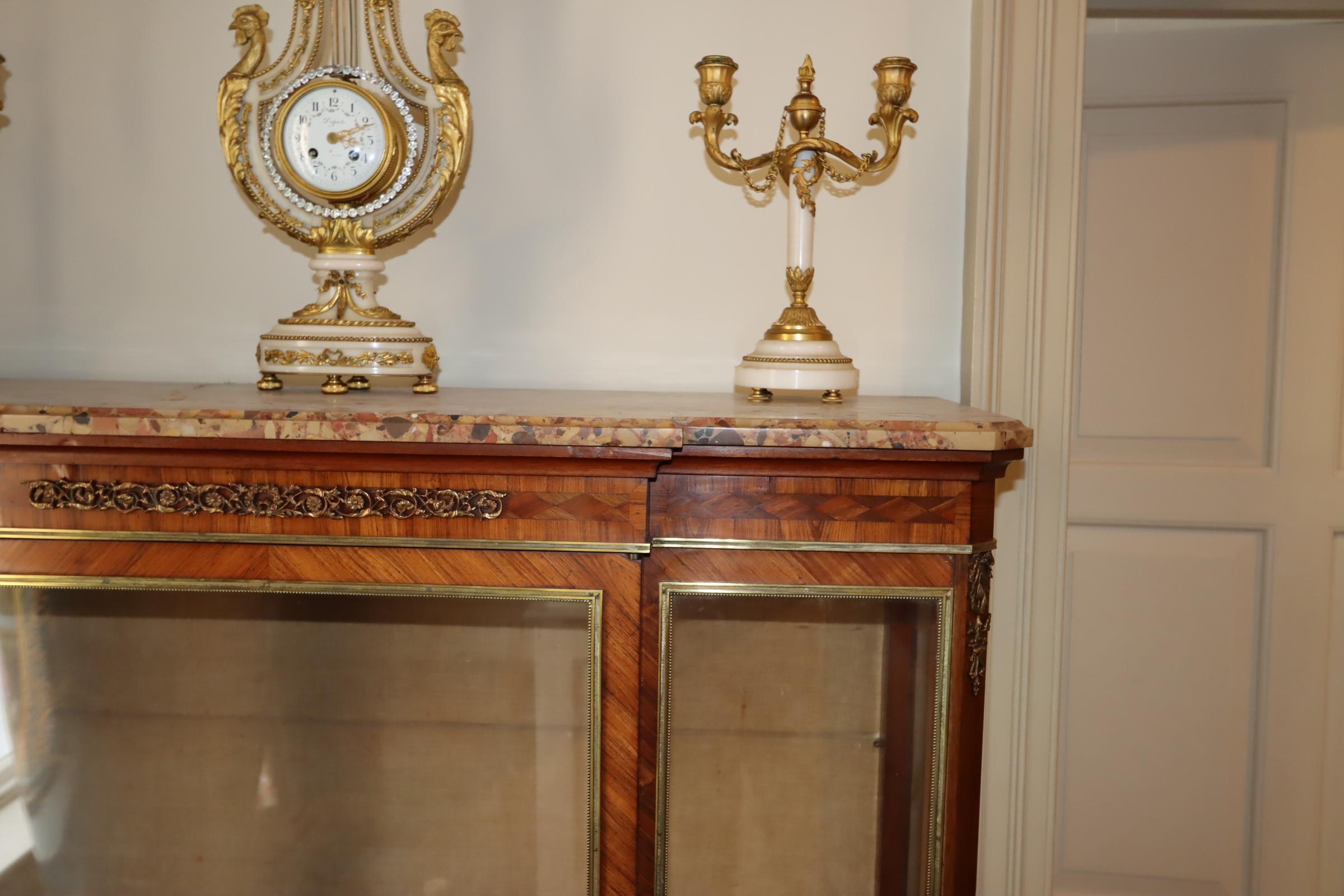 Exemplifying the exquisite artistry of turn-of-the-century French design, this captivating display vitrine, crafted around 1900, showcases the harmonious blend of kingwood and lavish ormolu mounts. The rich tones of kingwood veneer create a warm