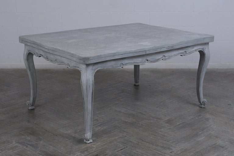 This late 19th-century French Louis XV-style dining table made of walnut wood has been professionally restored and features a wide rectangular top with carved wood moldings details around a newly painted grey and oyster color with a distressed