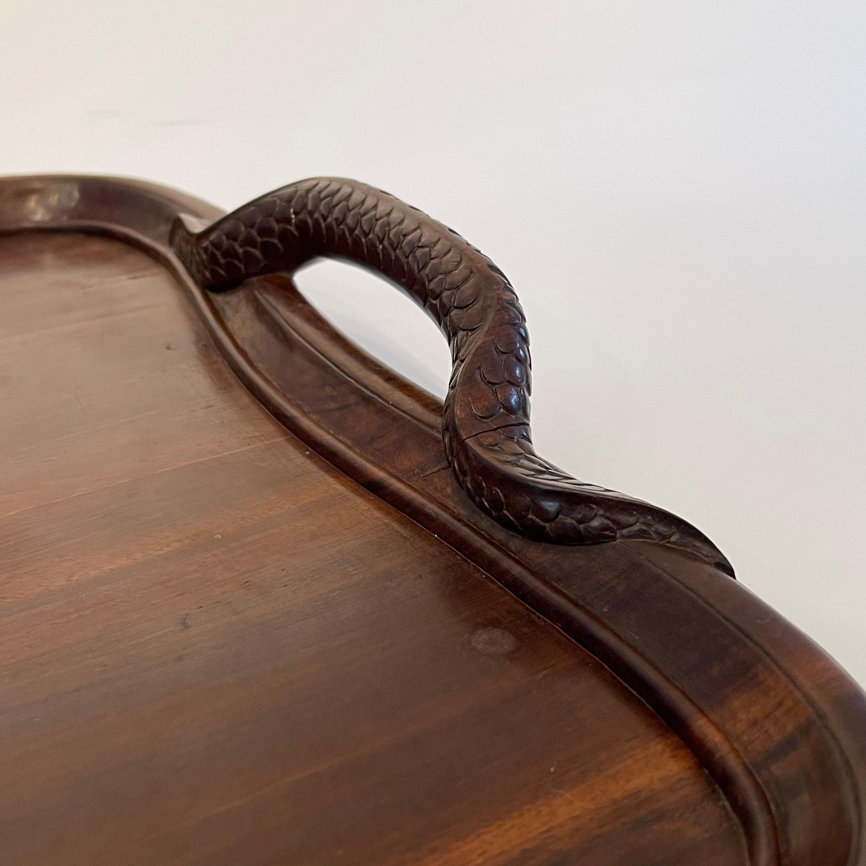 A beautiful hand carved double headed dragon tray with curved edges and two raised handles in the form of a dragon tail, the tail detailed with carved scales and fins snakes around the rim of the tray.