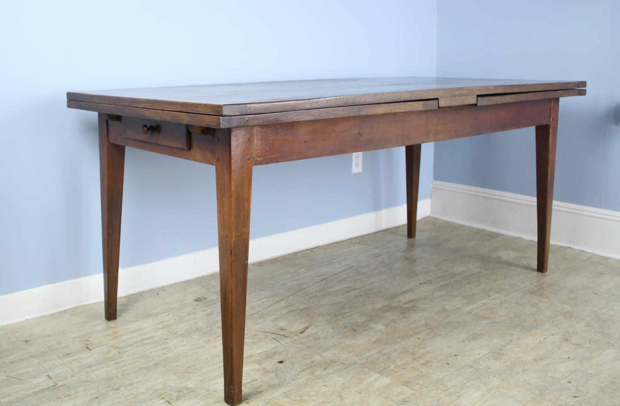 A pretty oak and chestnut dining or farm table from France, with Classic design details -tapered legs and a single drawer at one end - with a twist! This table extends to 132.5 inches - over 11 feet long, when both 31 inch draw leaves are extended.