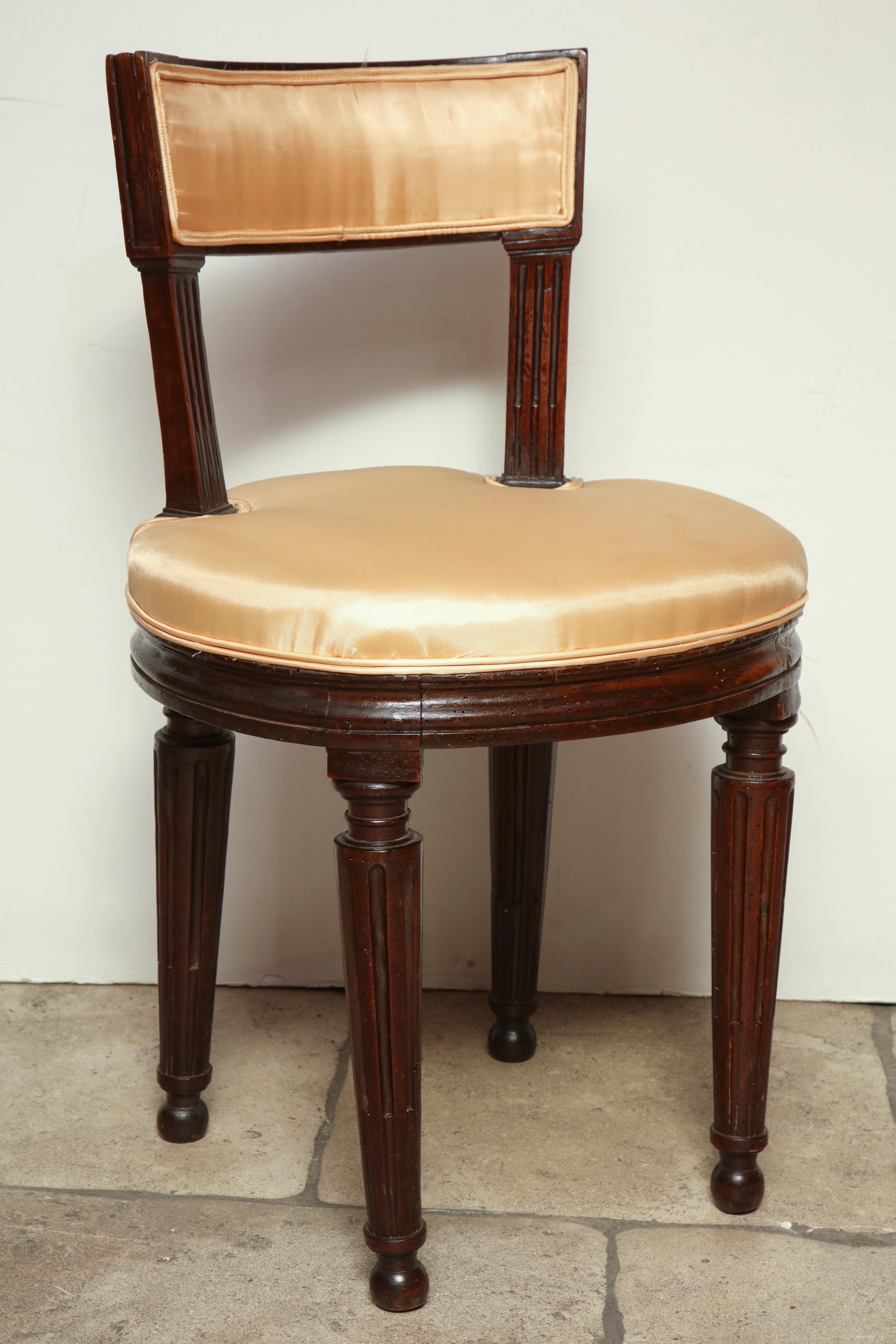 French Louis XVI walnut dressing stool in the Jacob manner, with molded and sides and fluted legs, with a round cushion seat and curved backrest.