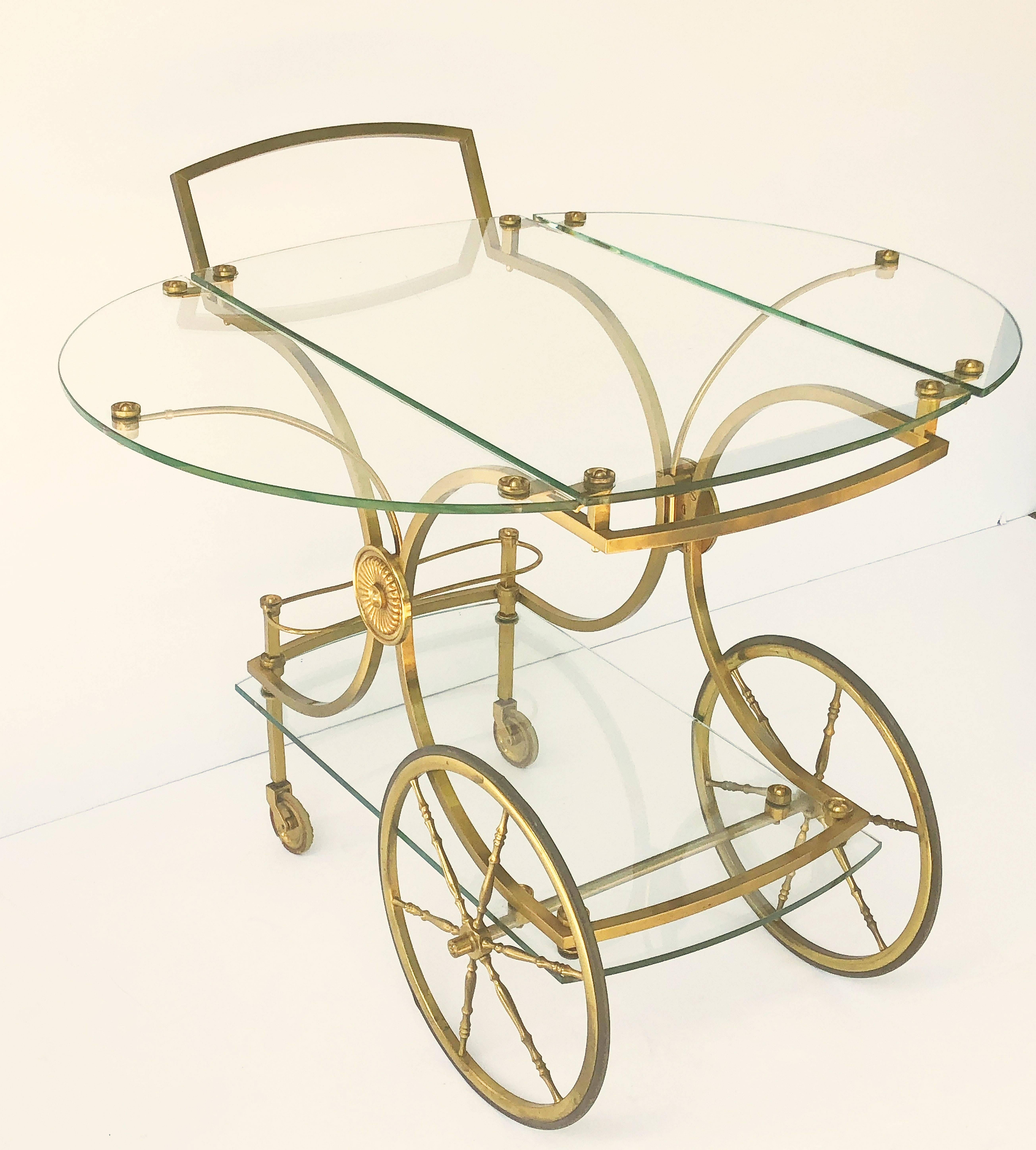 A fine French drinks cart or trolley (bar cart) of bronzed brass and glass by the celebrated Maison Charles, featuring an elegant brass X-frame design decorated with brass rosettes, supporting two glass tops.
There are two supports which swing out