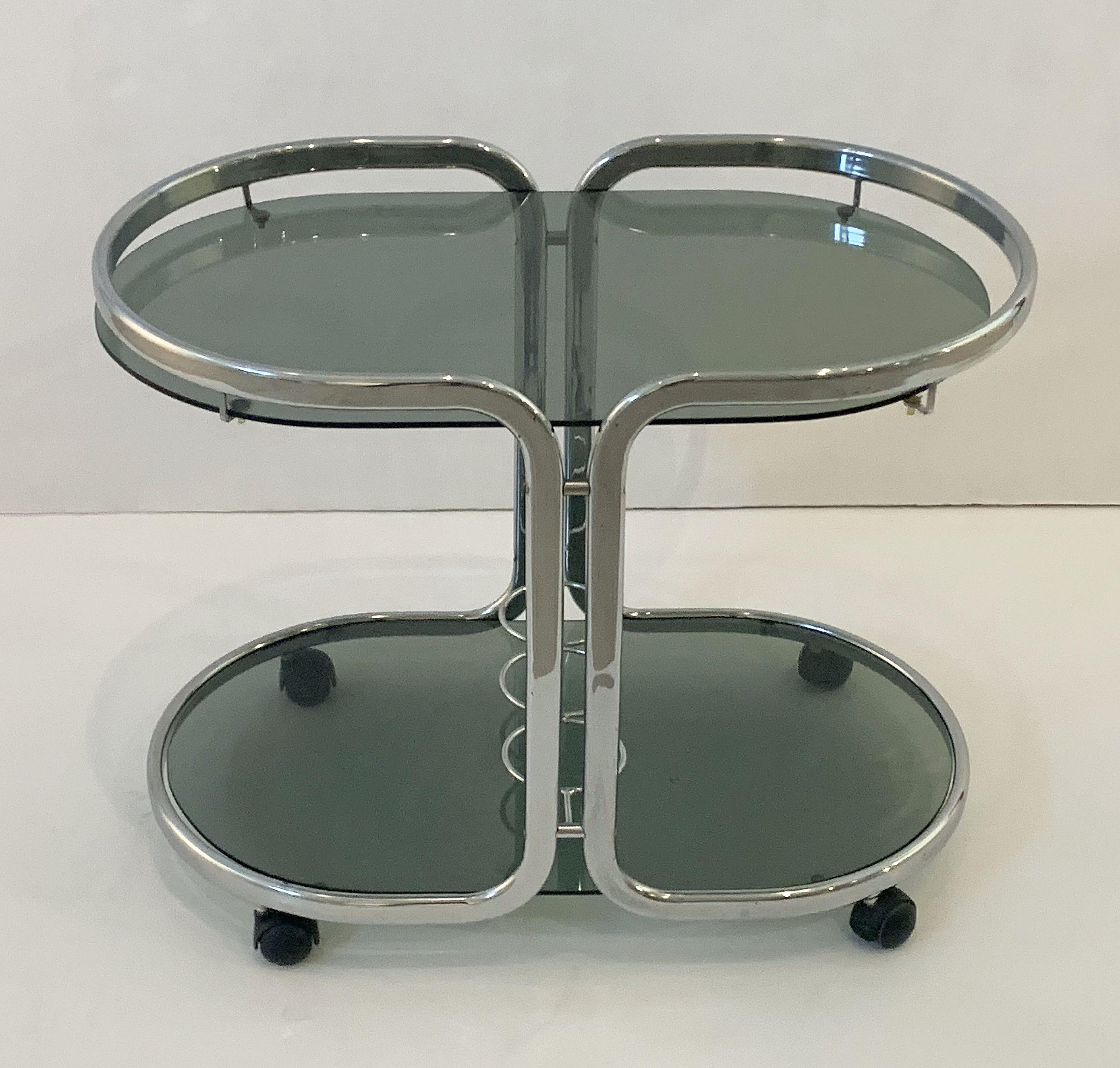 A handsome vintage French ovoid drinks cart table or bar trolley of stylish polished chrome, with two smoked glass shelves, bottle holder rack on bottom shelf, and set upon rolling casters.

 