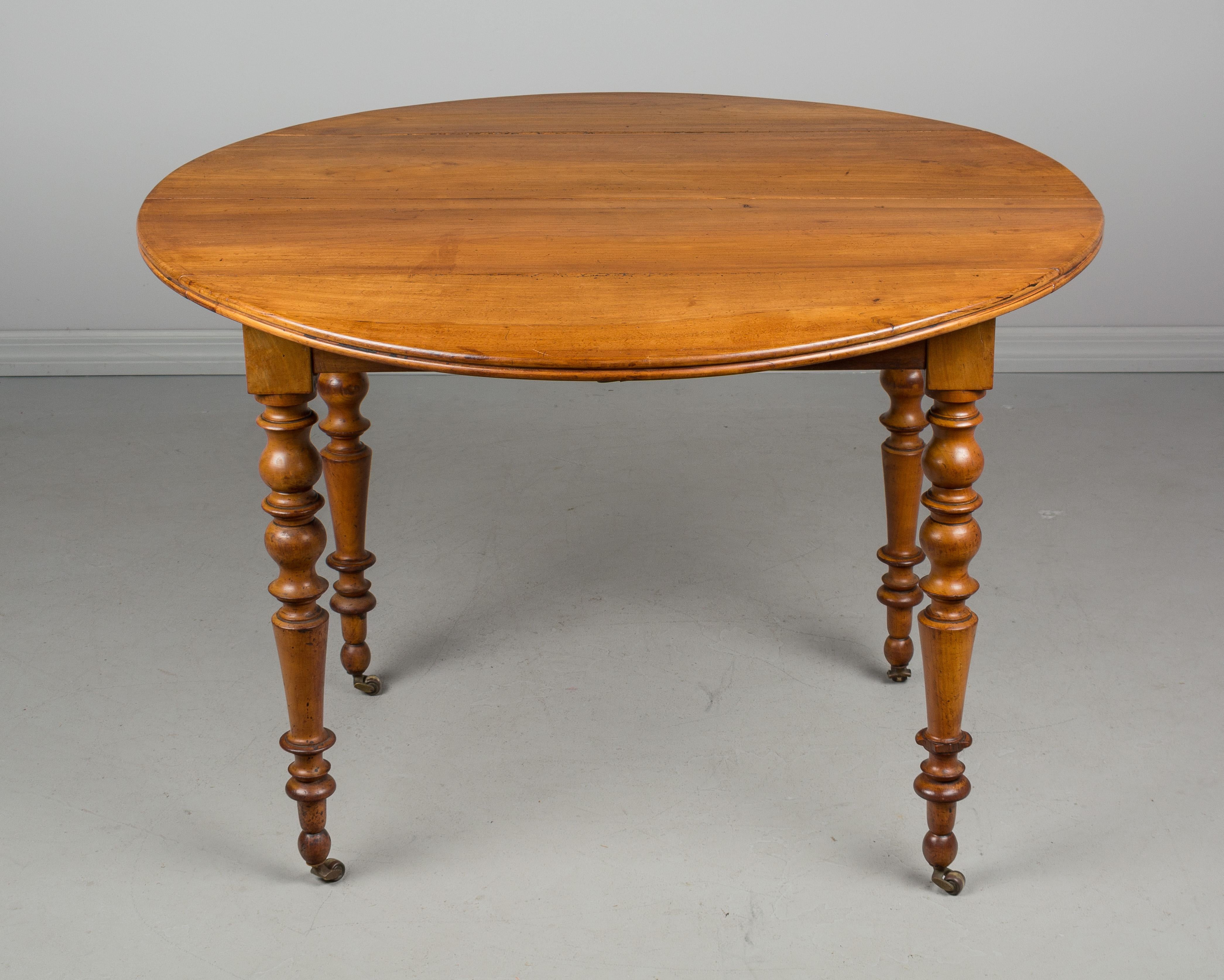 A Louis Philippe style drop-leaf dining table from Normandy. Made of cheerywood with four turned legs on brass castors. Wood has beautiful honey color with waxed finish. New runner for the extensions but no leaves for the table (extends to 79