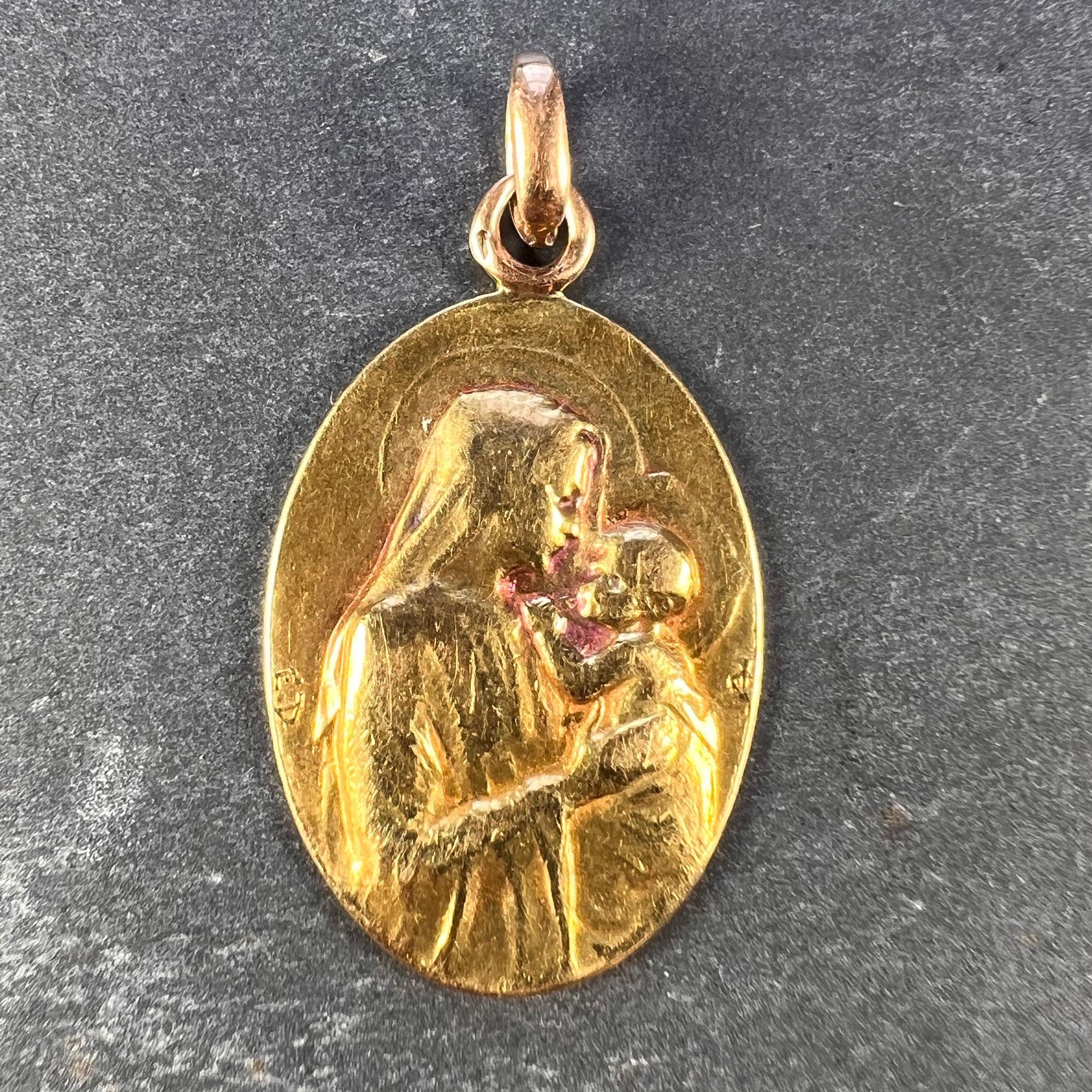 A French 18 karat (18K) yellow gold charm pendant designed as an oval medal depicting the Madonna and Child, signed and initialled by E. Dropsy. The reverse depicts a spray of lilies and the phrase 'Alma Mater' (Nourishing Mother) and is engraved