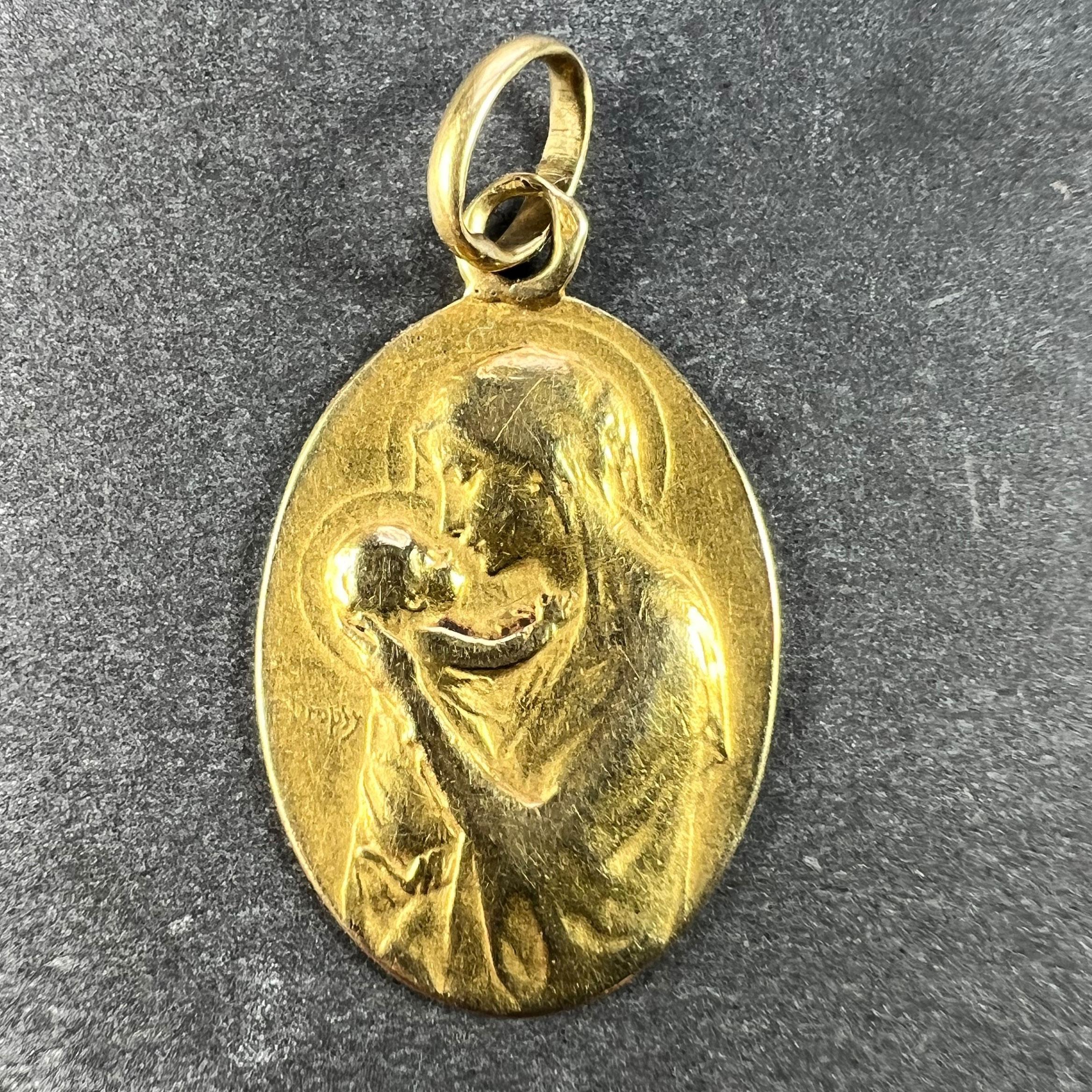 A French 18 karat (18K) yellow gold charm pendant designed as an oval medal depicting the Madonna and Child, signed E. Dropsy. The reverse depicts a spray of roses and lily of the valley and the phrase 'Mater Dei' (Mother of God) and is engraved