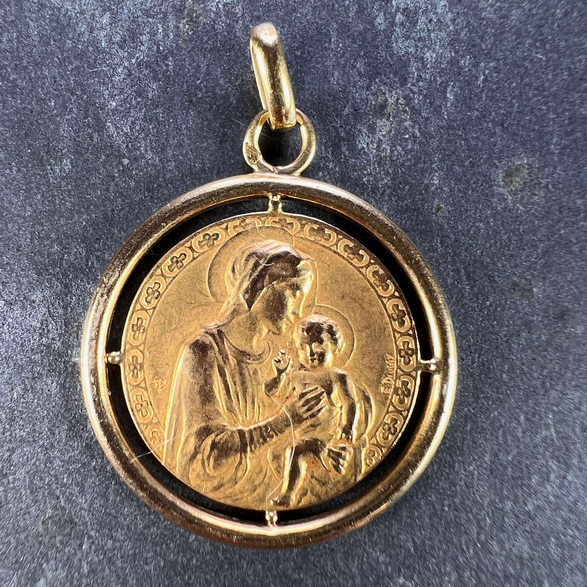 A French 18 karat (18K) yellow gold charm pendant designed as a medal depicting the Madonna and Child within a border of quatrefoils signed by E. Dropsy, surrounded by a yellow frame. The reverse features a rose in full bloom and is engraved with