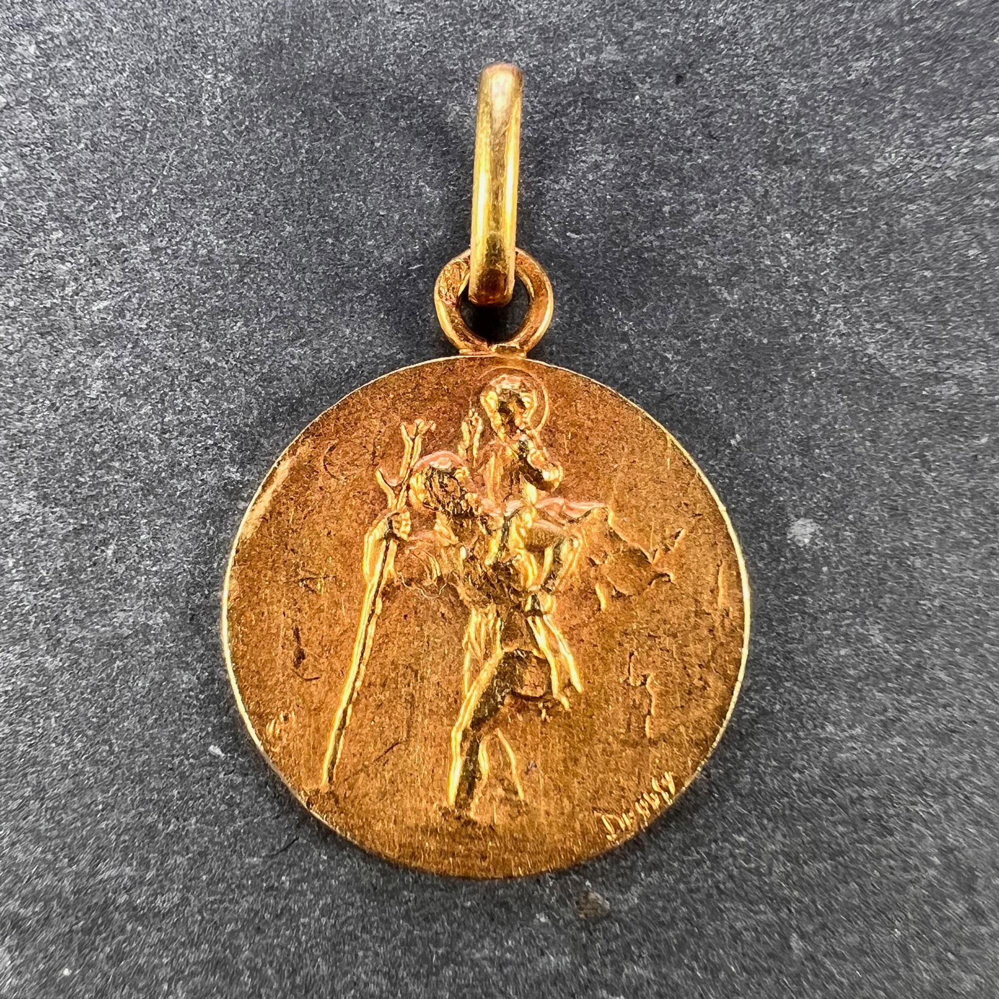 A French 18 karat (18K) yellow gold charm pendant designed as a disc representing Saint Christopher carrying the infant Christ. The reverse depicts a vintage car with the phrase 'Regarde Saint Christophe et va t'en rassure'. Engraved with the