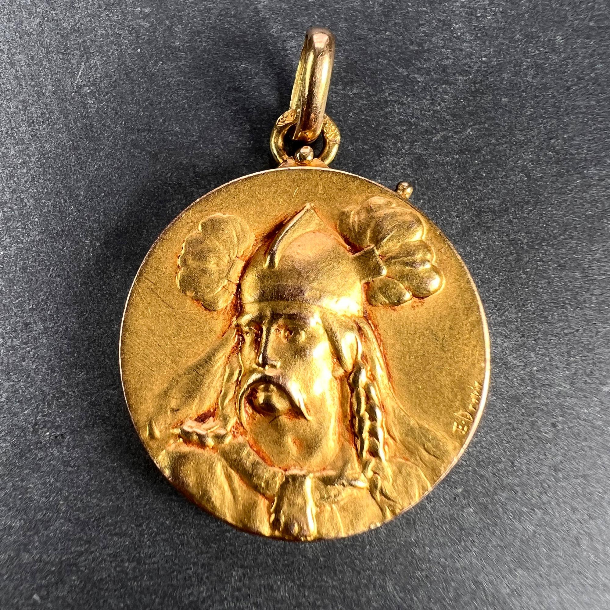 A French 18 karat (18K) yellow gold pendant locket depicting Vercingetorix the Gallian leader, to one side and a suit of armour, weapons and a flag to the other. Signed E. Dropsy. Stamped with the horse’s head  mark for 18 karat gold and French