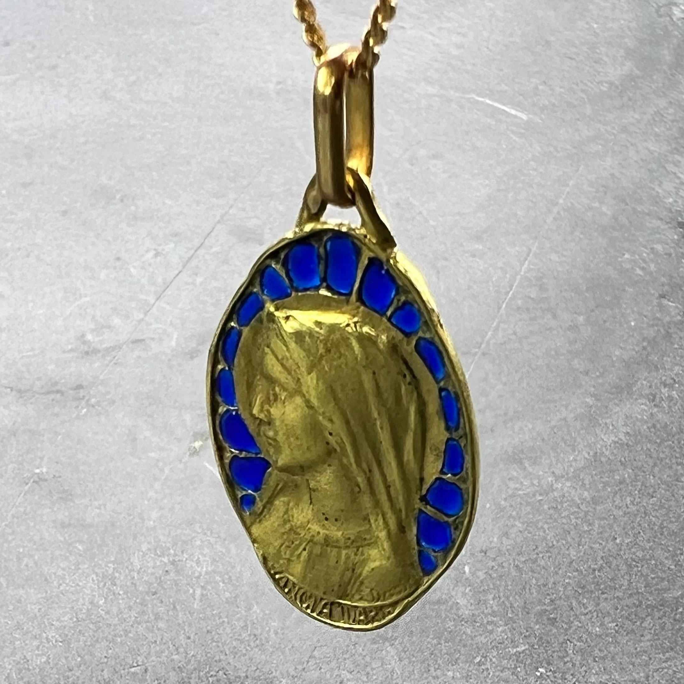 A French 18 karat (18K) yellow gold charm pendant designed as an oval medal depicting the Virgin Mary with plique a jour blue enamel surround, over the words 'SANCTA MARIA'. Partially engraved to the reverse with the date '10 Juillet 1932'. Signed E