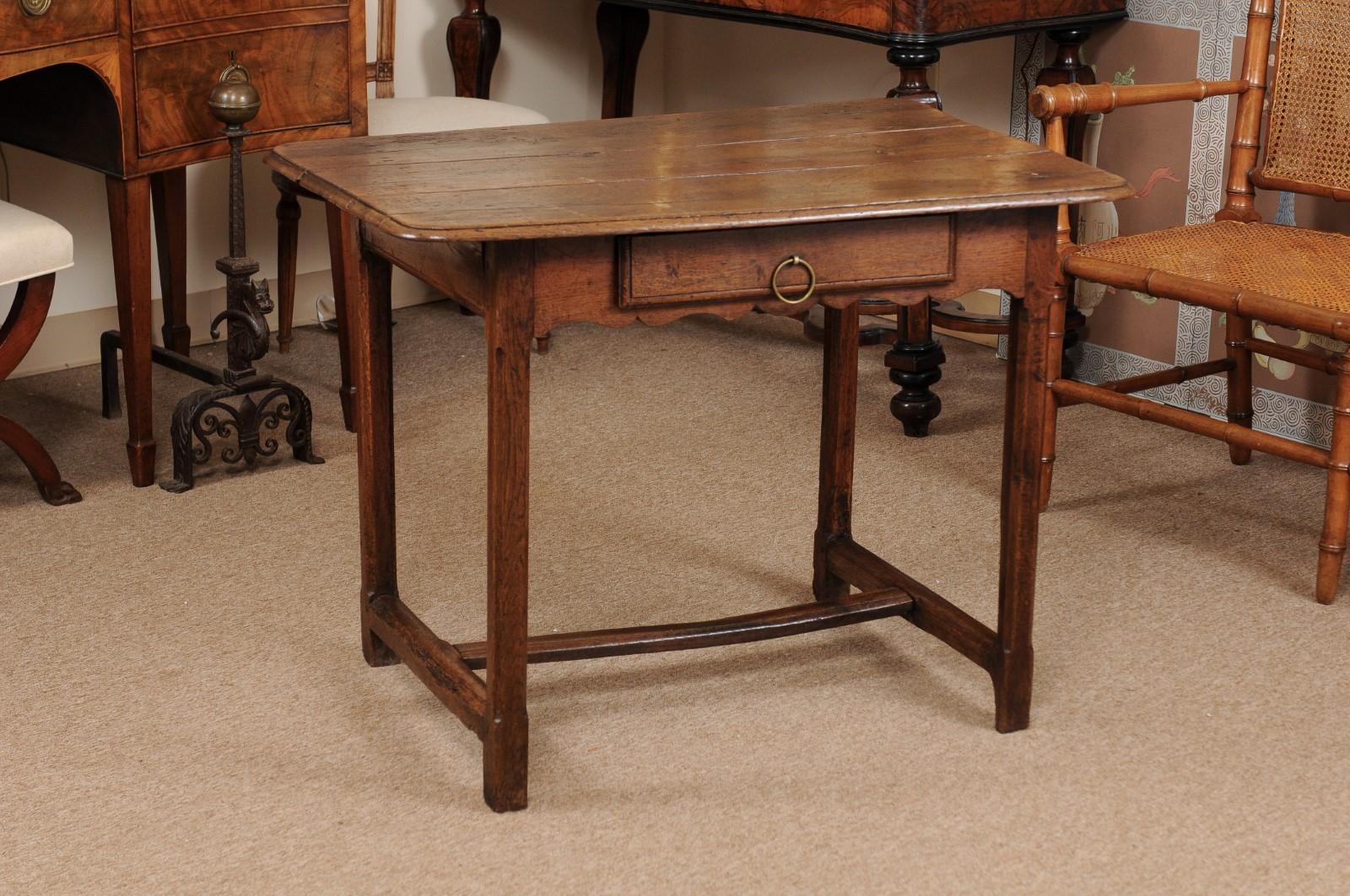 The early 18th century French oak side table with 3-piece rectangular top with molded edge, drawer below and carved shaped apron ending in square legs joined with stretcher.