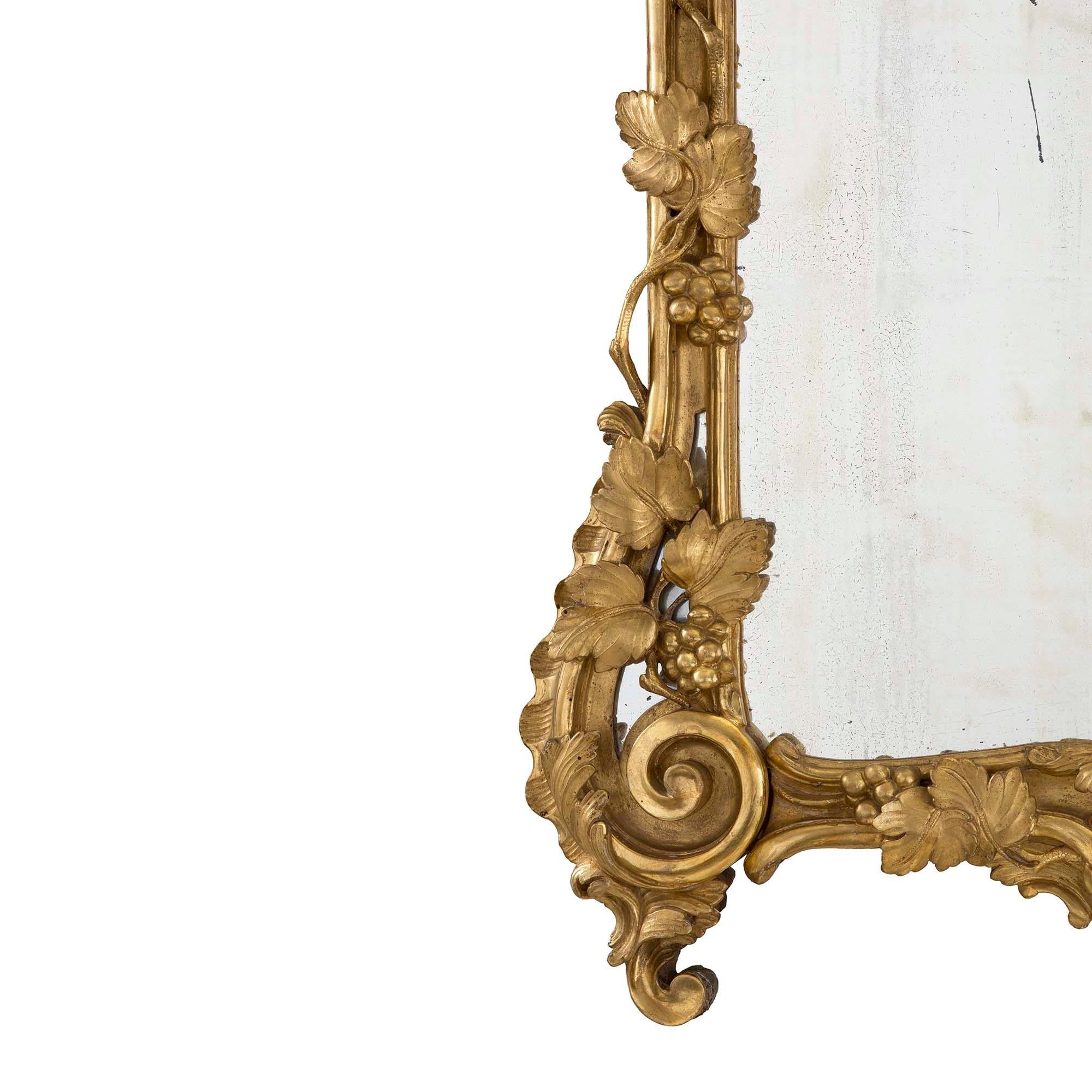 A charming French early 18th century Regence period giltwood mirror circa 1720. The original mirror plate is framed within a wonderfully detailed and richly carved giltwood border displaying beautiful scrolled movements and Fine grape leaves and