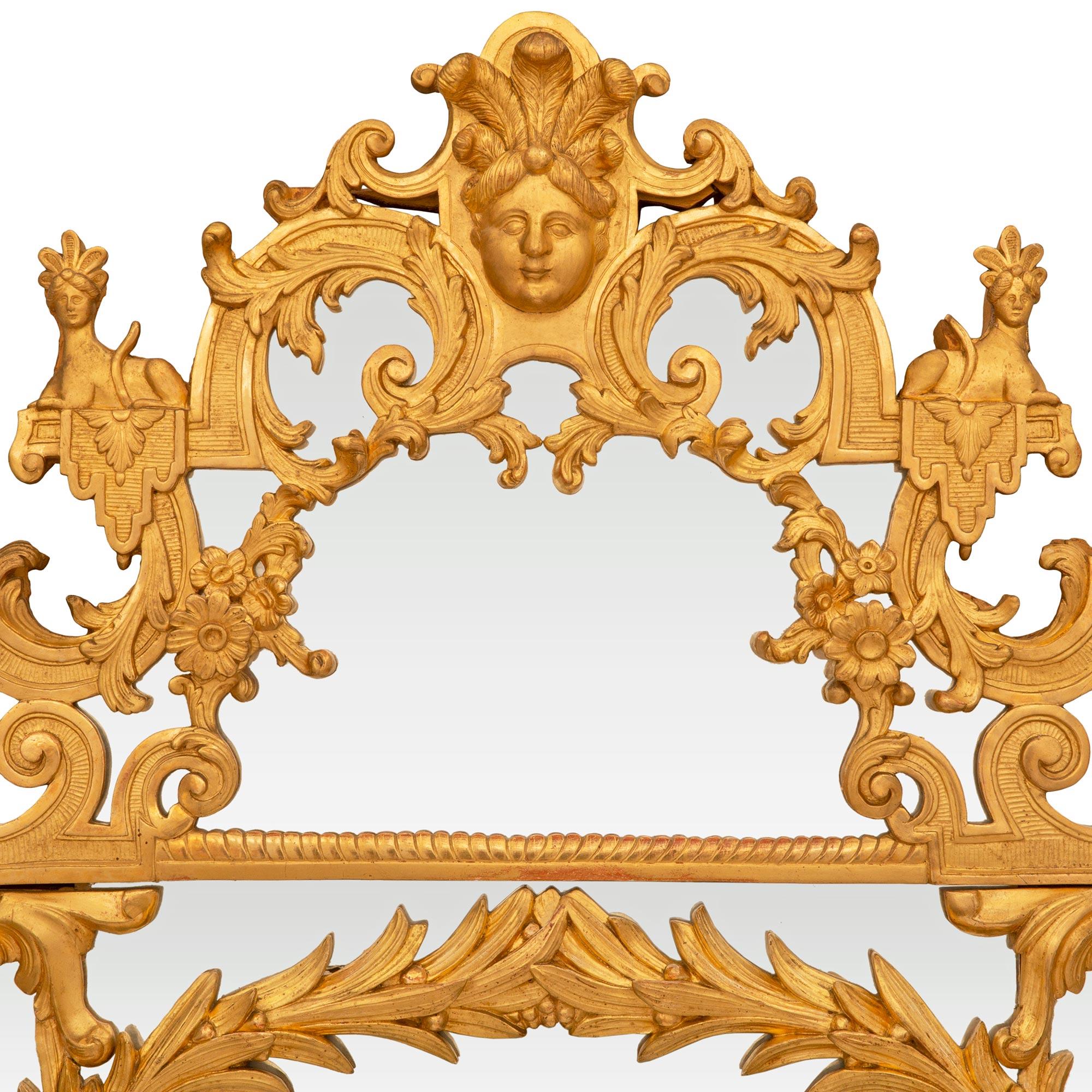 Superbe miroir en bois doré de la période Régence du XVIIIe siècle. Le miroir à double encadrement est décoré d'opulentes volutes et feuilles en bois doré. Au sommet, on trouve des masques de théâtre au milieu de rinceaux, de guirlandes et de